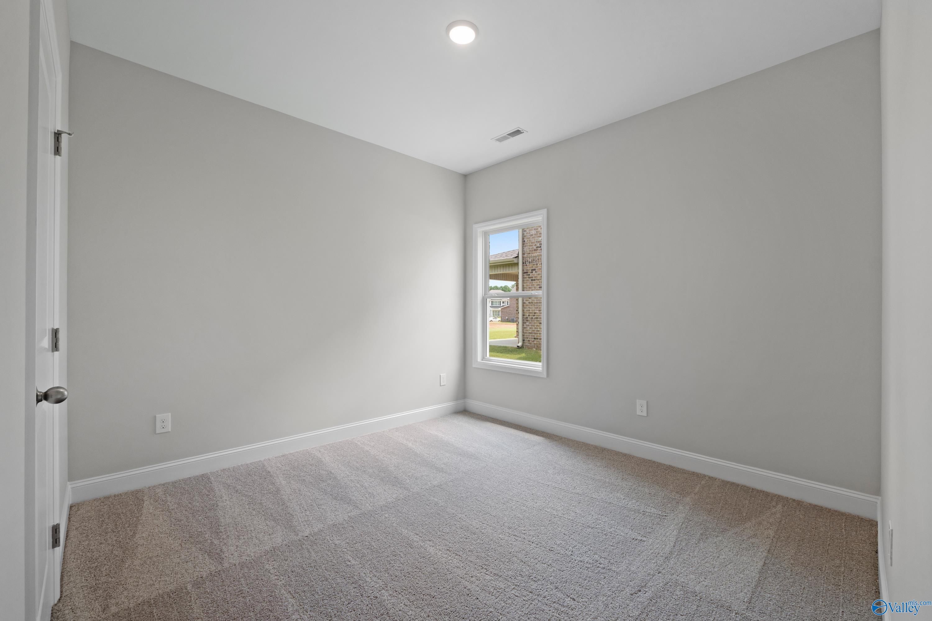 Bright bedroom with light gray walls, beige carpet, and window overlooking yard in Davidson Homes The Franklin C, Harvest, AL