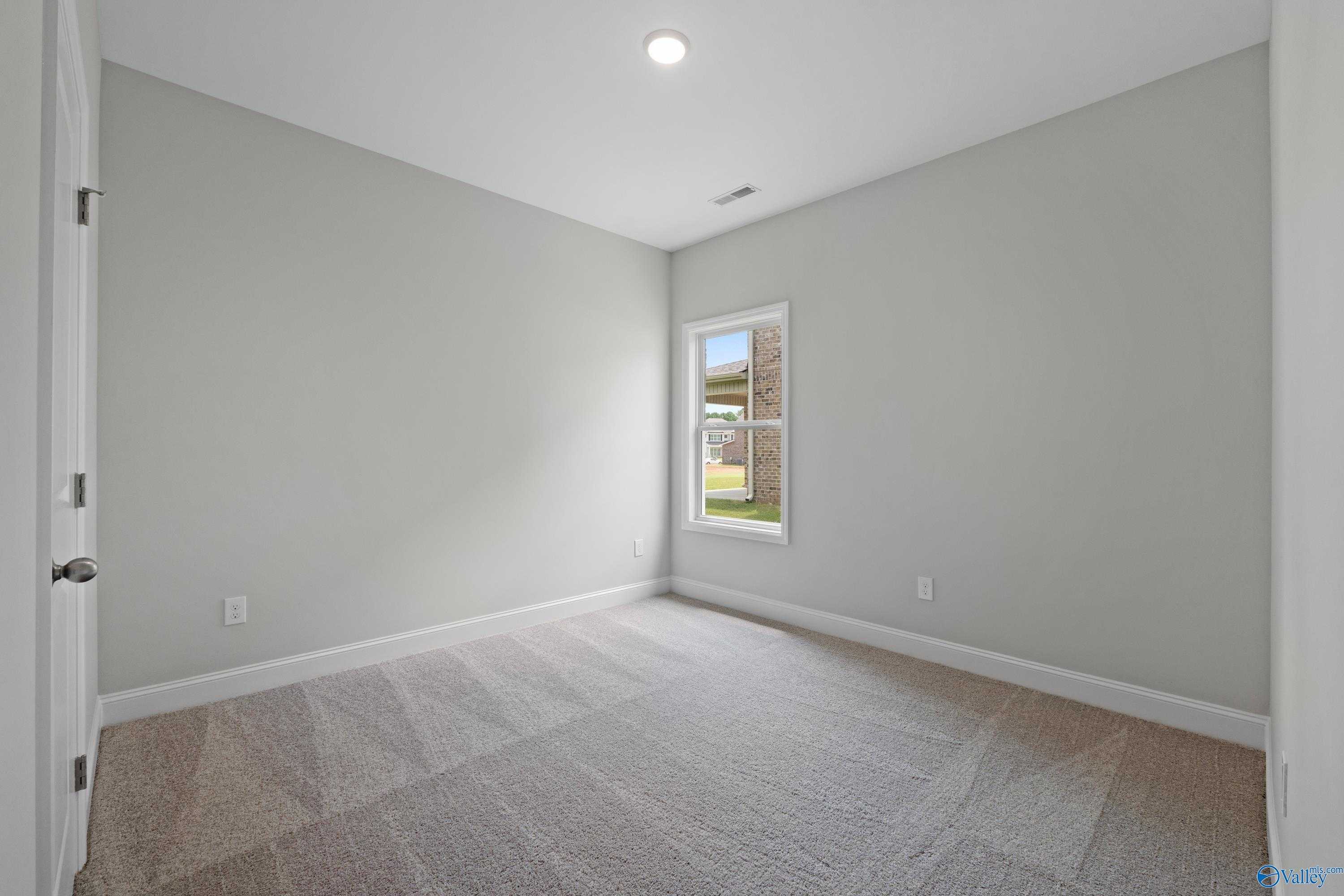 Bright bedroom with light gray walls, beige carpet, and window overlooking yard in Davidson Homes The Franklin C, Harvest, AL