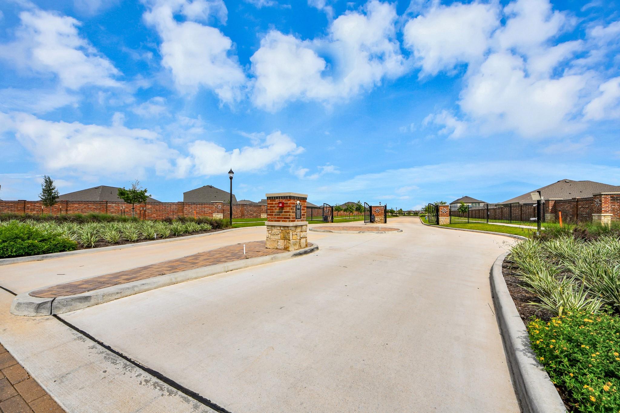 Gated community entrance with brick columns and landscaping at Sunterra master-planned community in Katy, Texas.