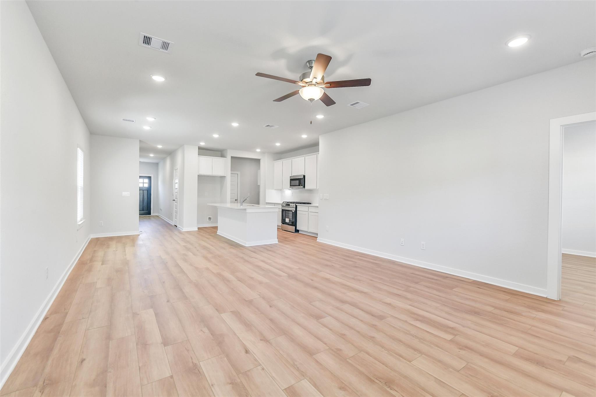 Open-concept kitchen and living area with white island, stainless appliances, hardwood floors, and ceiling fan in Davidson Homes The Blanco E, Magnolia, Texas