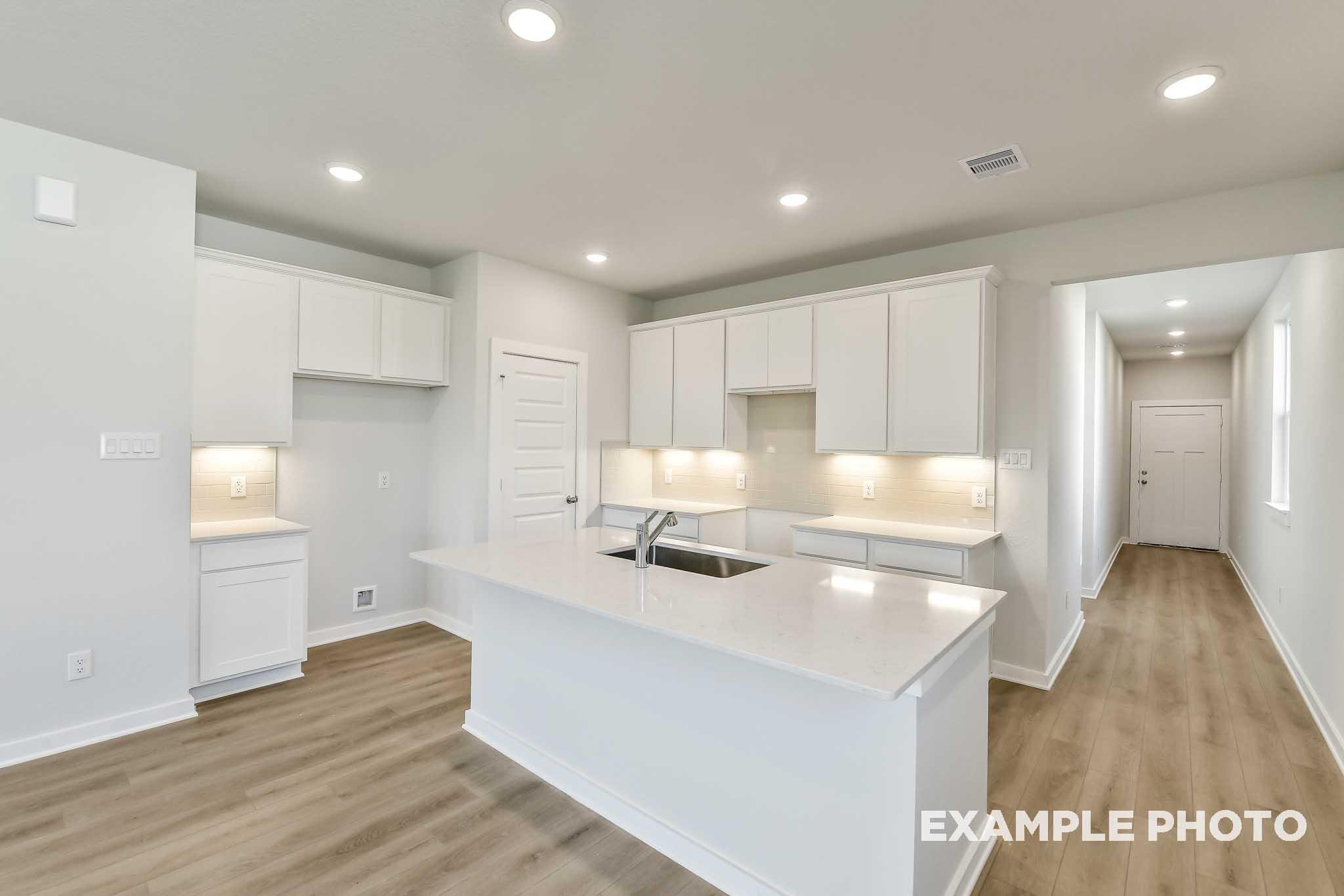Bright kitchen with large white island, quartz countertops, white cabinetry, and wood-look flooring in The Colorado by Davidson Homes