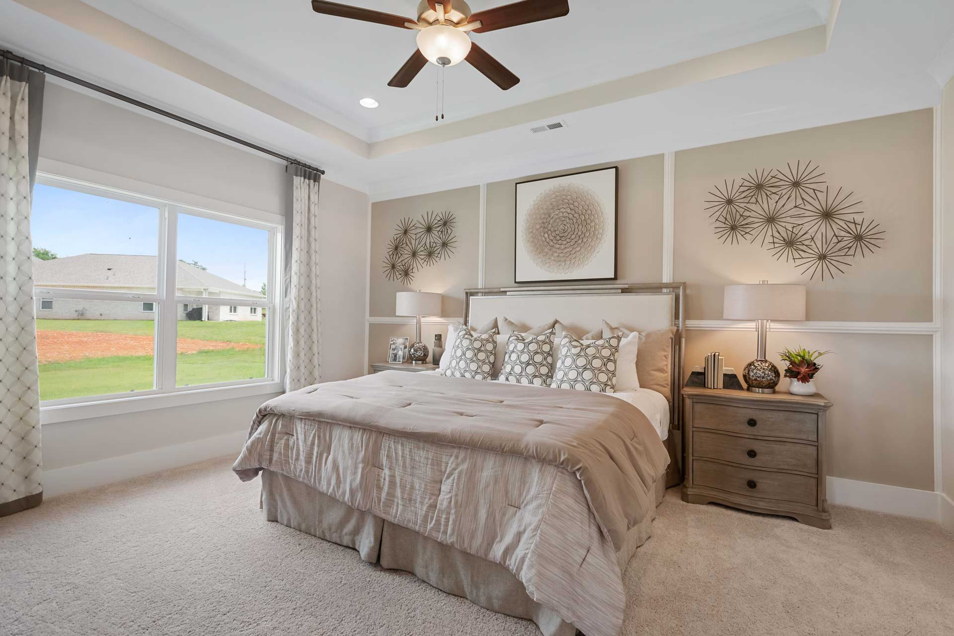 Spacious master bedroom at Flint Meadows in New Market AL with king bed, neutral tones, ceiling fan, large windows and wall art