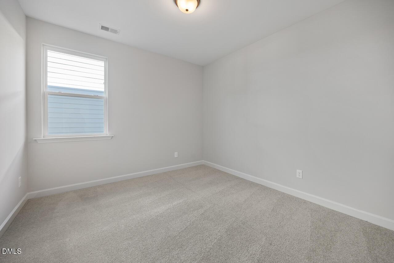 Bright empty bedroom with plush carpet, neutral walls, and window in Davidson Homes The Preston C, Wendell Ridge, NC