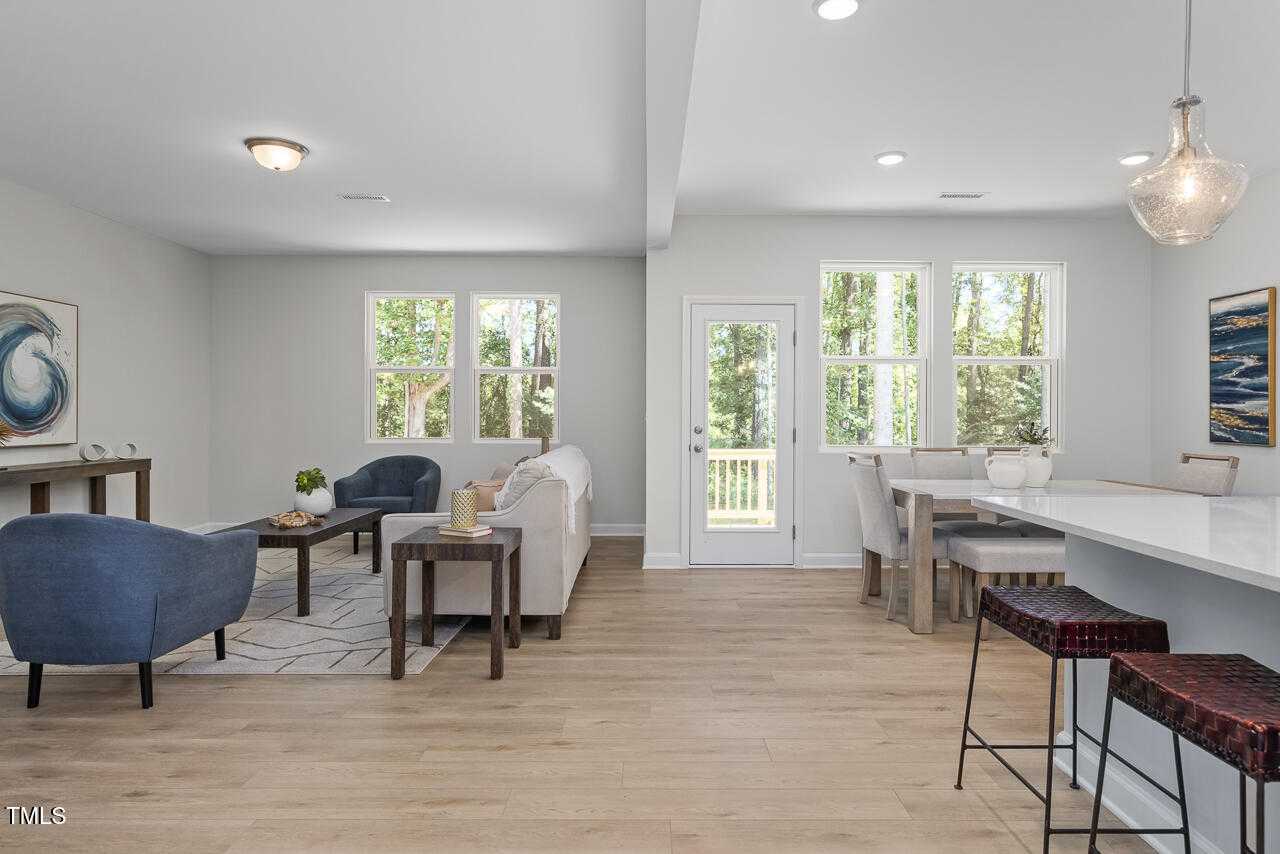 Open-concept living room with sofa, dining table, and kitchen island overlooking deck in Davidson Homes Willow C, Lillington, NC