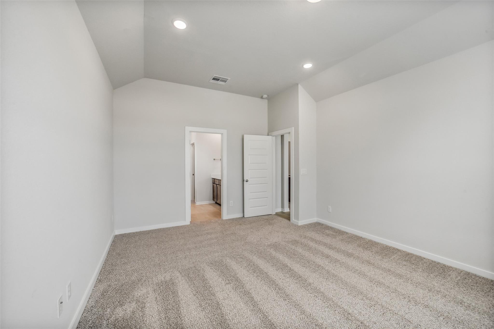 Spacious secondary bedroom with en-suite bath door, beige carpet, and recessed lights in Davidson Homes The Acadia C, Magnolia TX