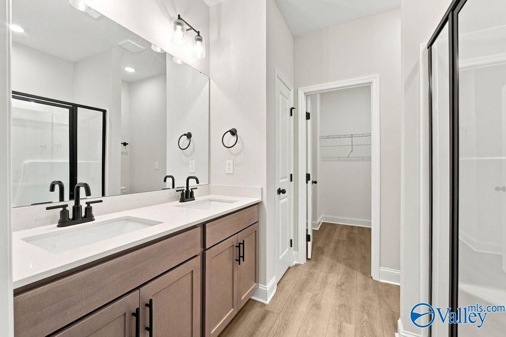 Modern master bathroom with dual vanity, wood-look flooring, and walk-in closet in The Camilla C home at Cain Park.