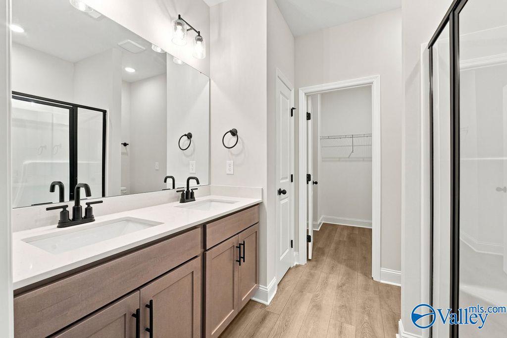 Modern master bathroom with dual vanity, wood-look flooring, and walk-in closet in The Camilla C home at Cain Park.