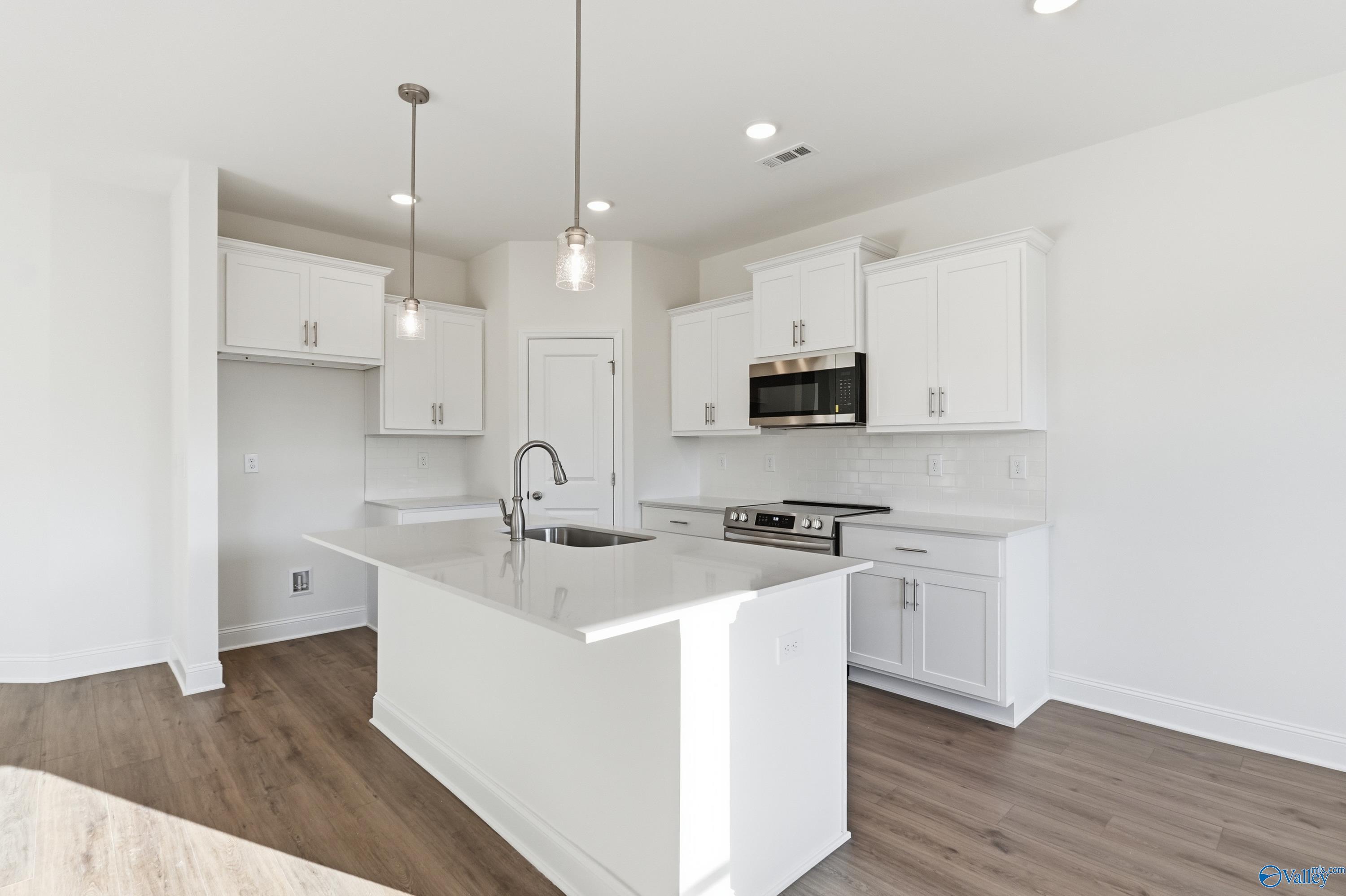 Modern white kitchen with spacious island sink, stainless steel appliances, and pendant lights in The Asheville C by Davidson Homes, Meridianville, AL