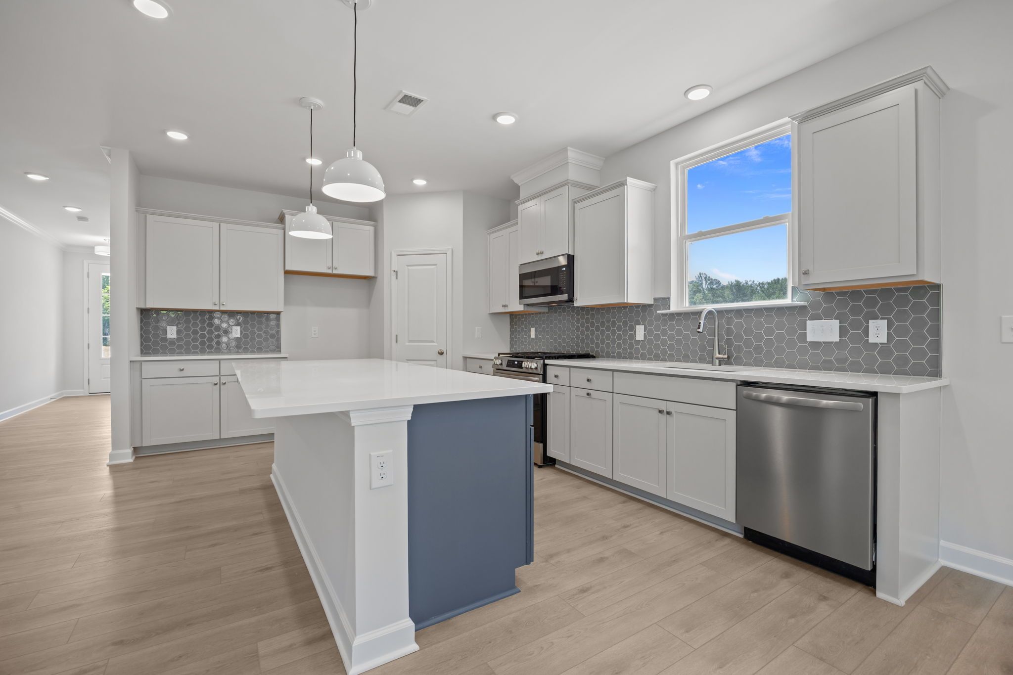 Modern kitchen in The Ashport B featuring a large blue island, light grey cabinets, and stylish hexagon tile backsplash.