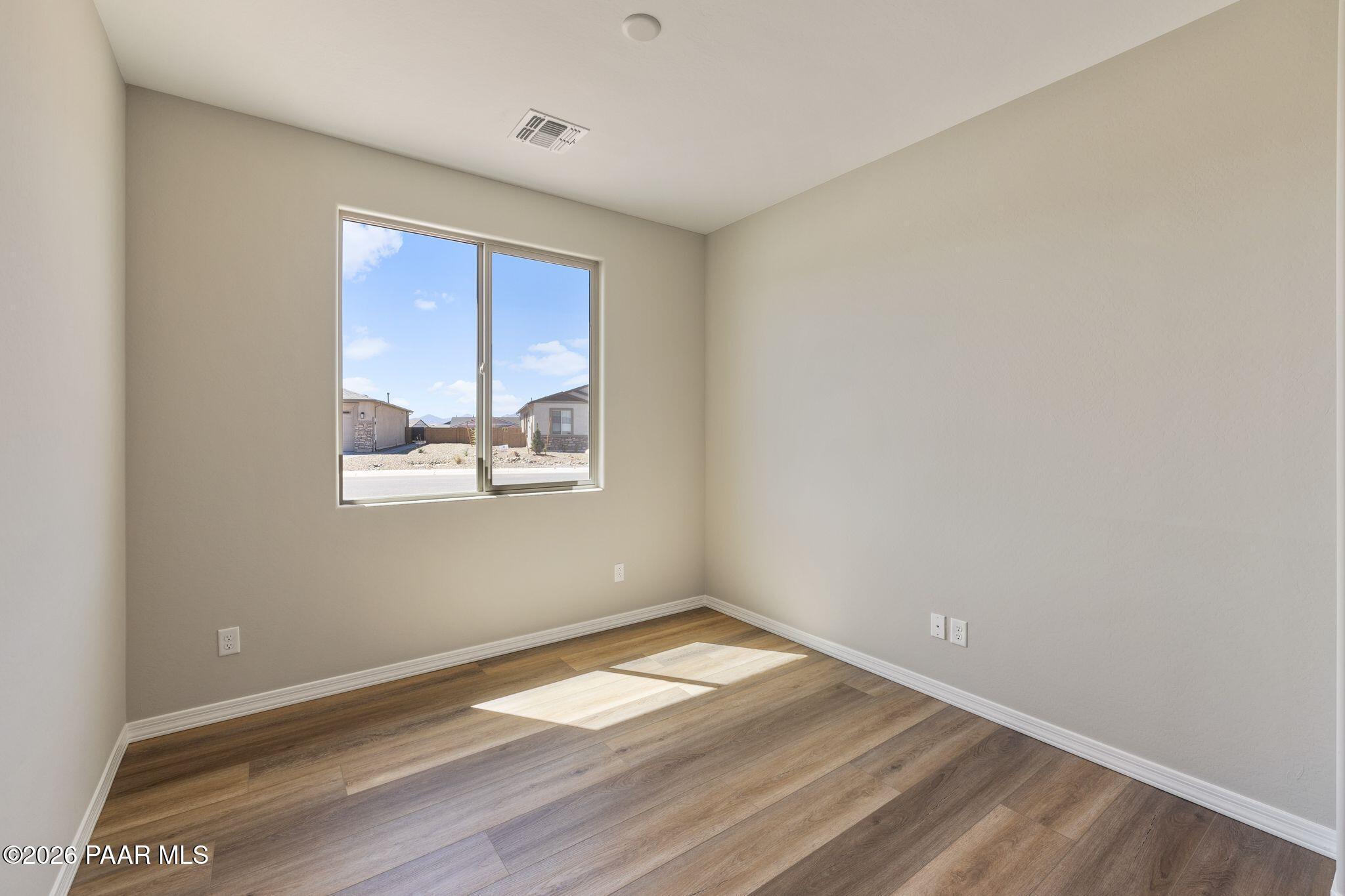 Bright bedroom with beige walls, large sunny window, hardwood floors in Davidson Homes The Frontier A, Prescott Valley, AZ