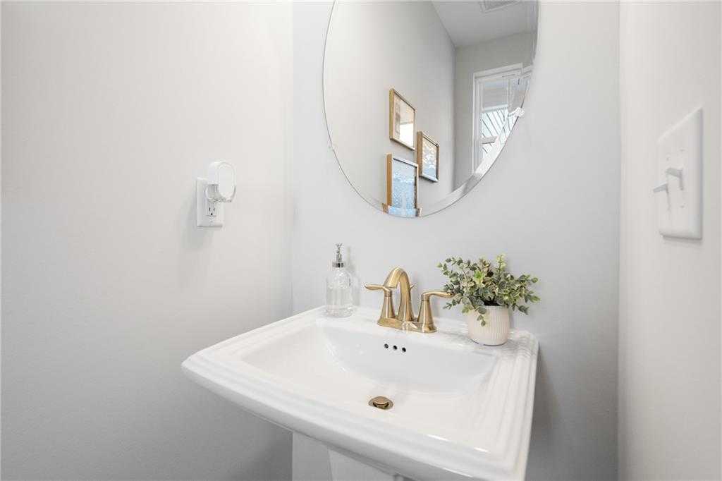 Elegant powder room featuring round mirror, white pedestal sink, gold faucet, soap dispenser and potted greenery in Wilmington B home, Emerson GA