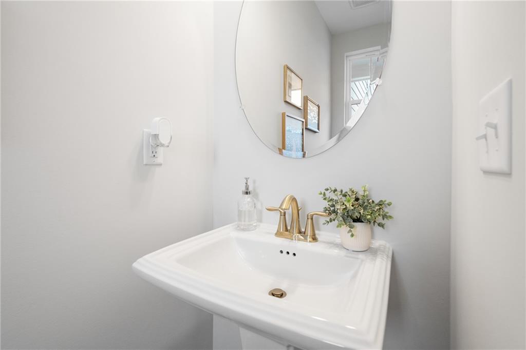 Elegant powder room with white pedestal sink, gold faucet, round mirror, and eucalyptus plant in Davidson Homes The Wilmington B, Emerson, Georgia