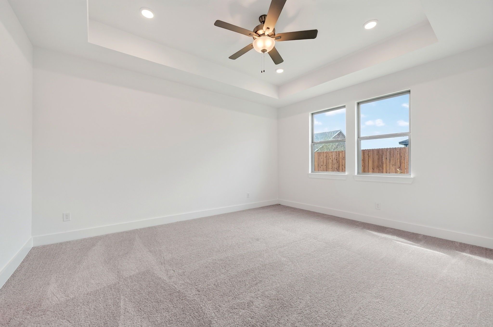 Bright bedroom with tray ceiling, ceiling fan, plush carpet, and large windows in Davidson Homes The Holly F, Josephine, TX