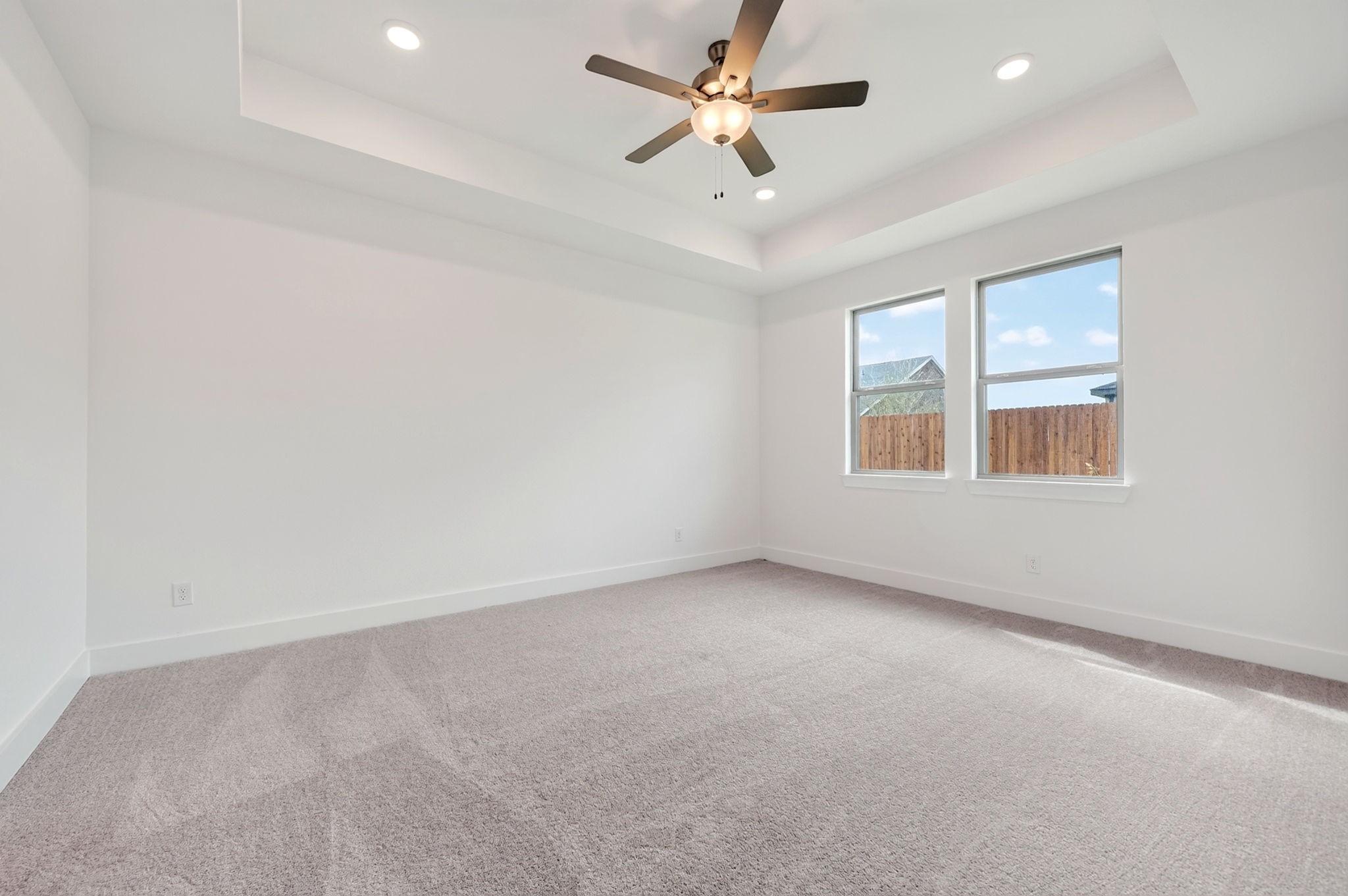 Bright bedroom with tray ceiling, ceiling fan, plush carpet, and large windows in Davidson Homes The Holly F, Josephine, TX