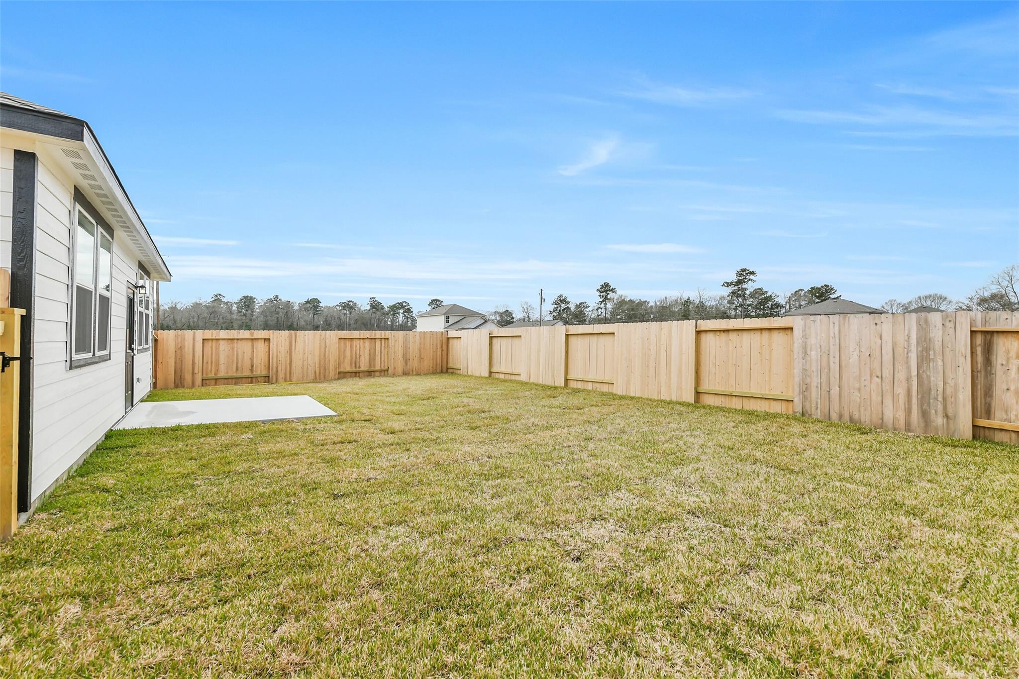 Fenced backyard with green lawn, concrete patio, and pine trees in Davidson Homes The Frio G, Liberty Estates, Cleveland, Texas