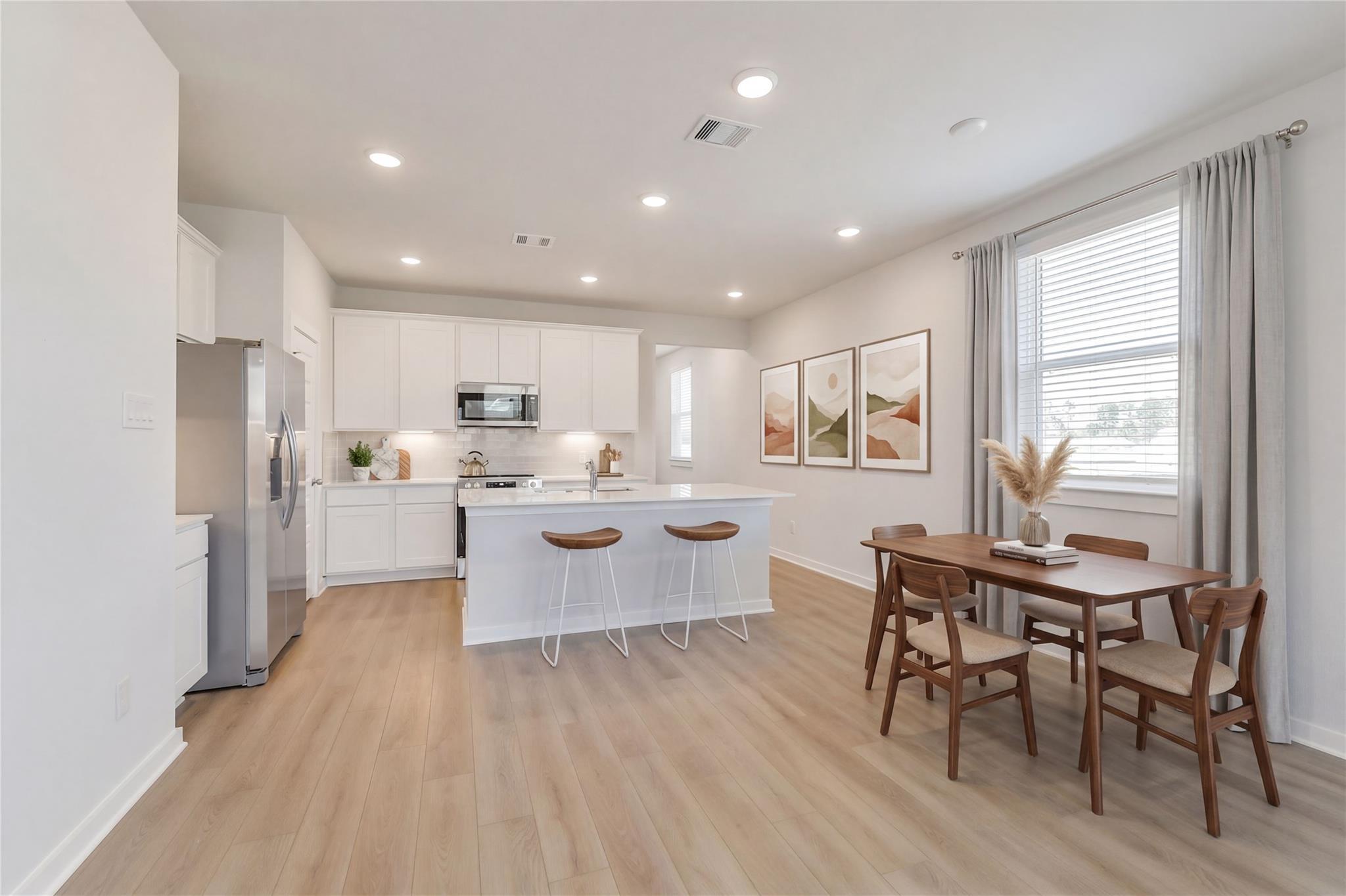 Modern open kitchen with white cabinets, stainless fridge, large island bar stools, and adjacent dining table in Davidson Homes The Colorado F, Cleveland, Texas