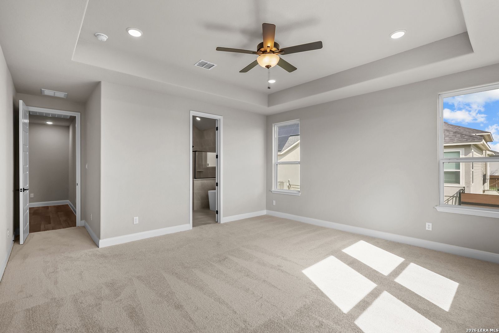 Bright primary bedroom with tray ceiling, ceiling fan, and carpet flooring in Davidson Homes The Foster E, Potranco Oaks, Castroville, TX