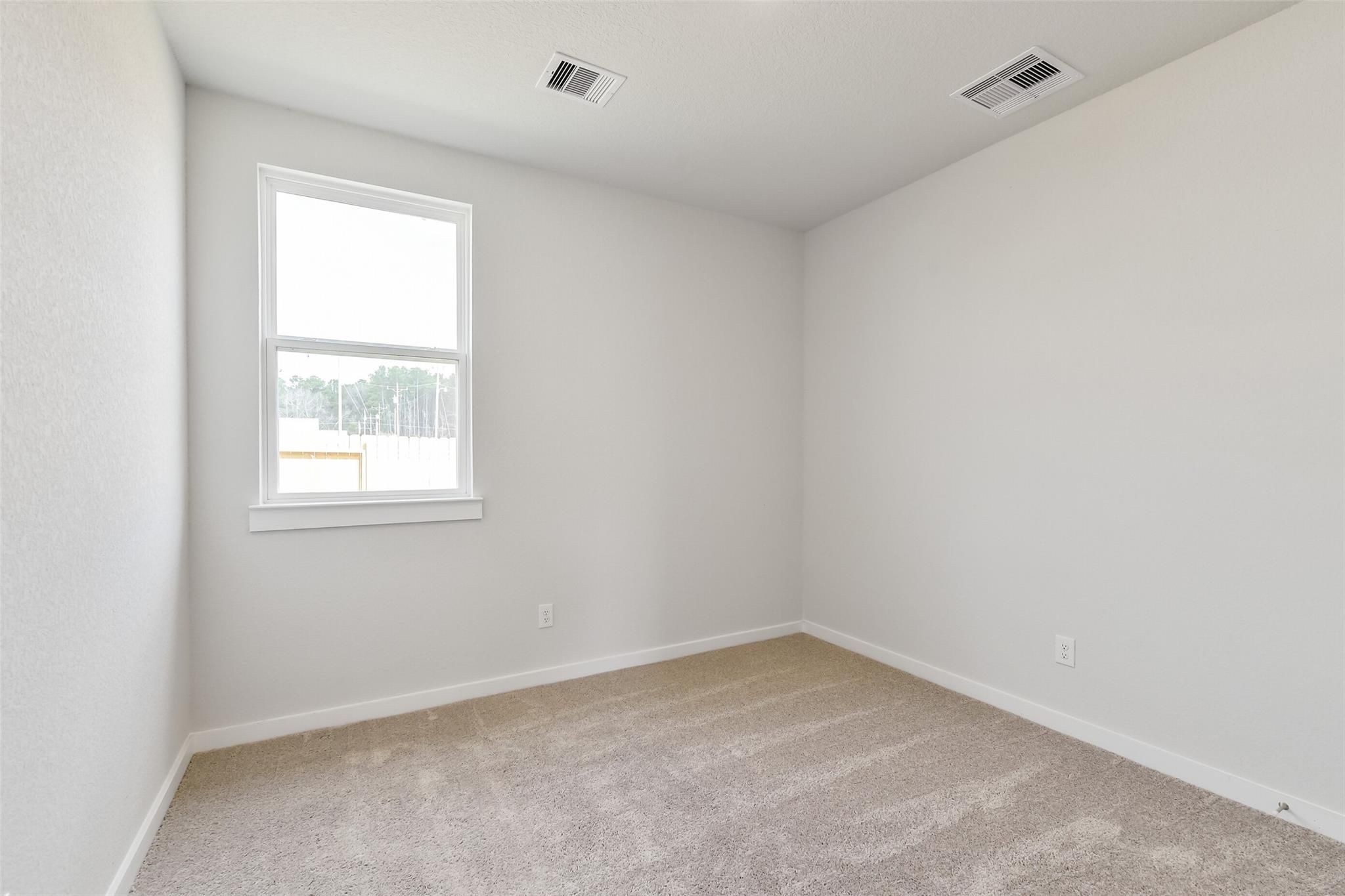 Bright empty bedroom with neutral walls, beige carpet, and window to wooded view in Davidson Homes The Frio G, Cleveland, Texas