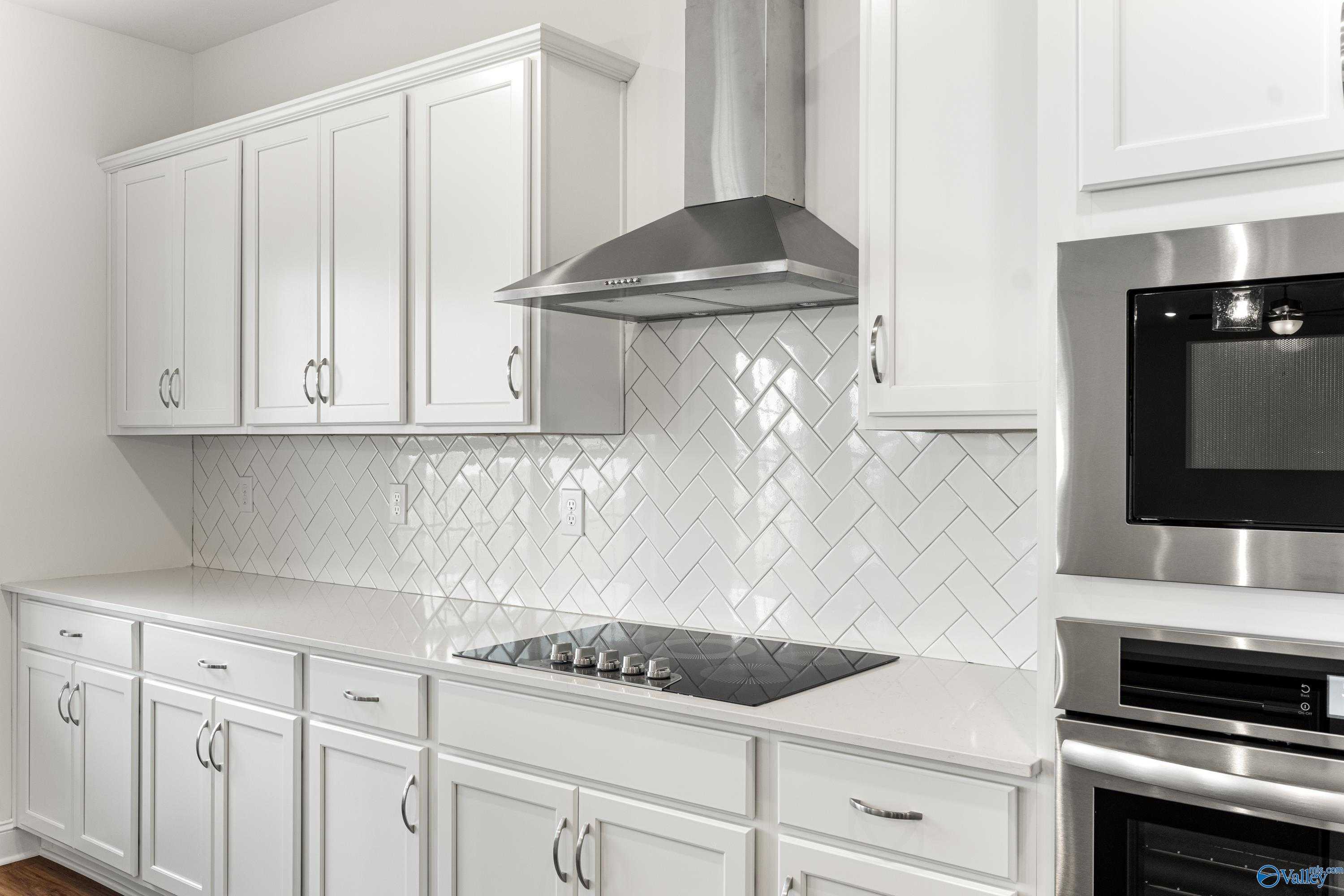 White kitchen with herringbone subway tile backsplash, quartz counters, stainless appliances in The Madison B by Davidson Homes, Meridianville, AL