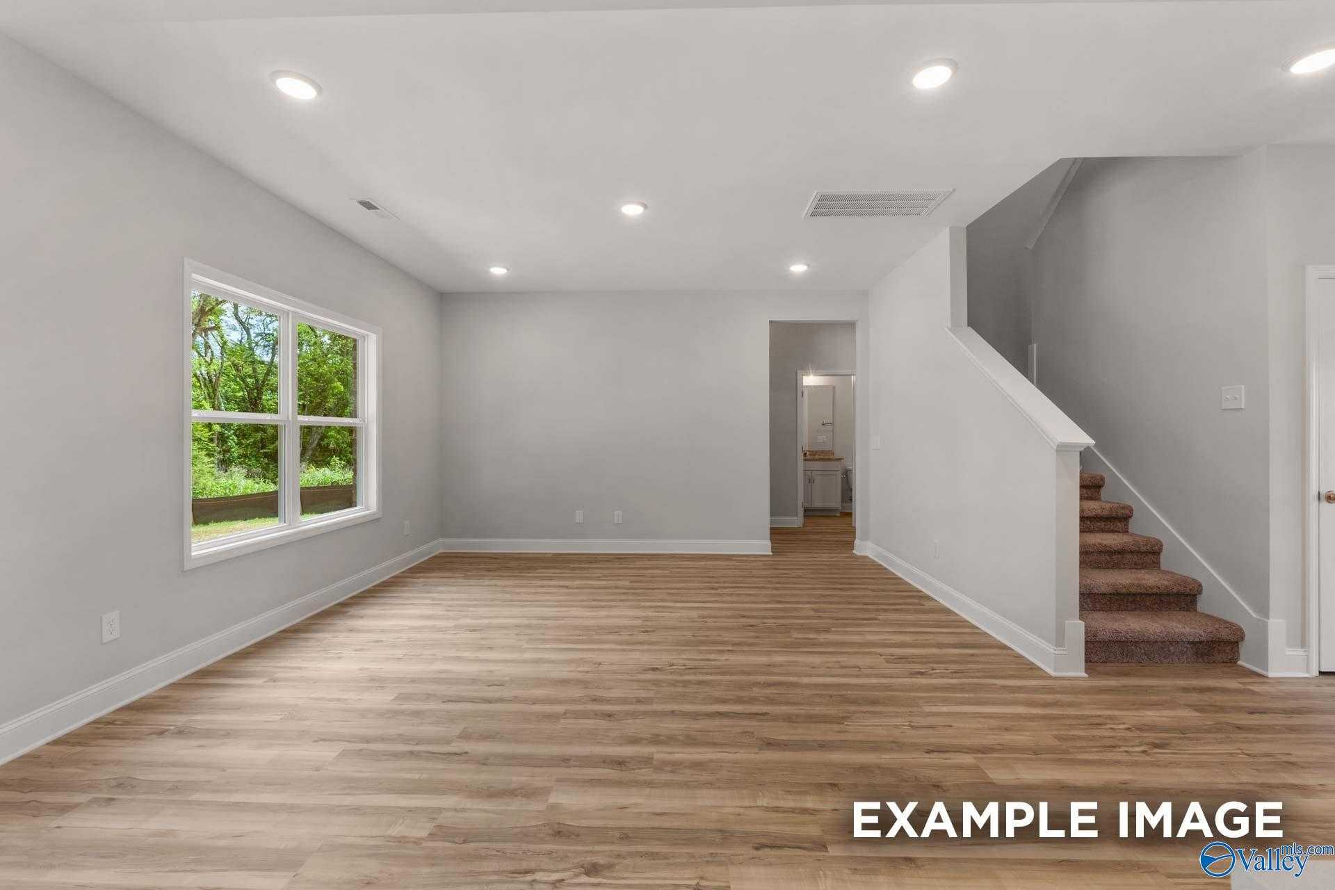 Bright open living room with hardwood floors, large windows, recessed lights, and carpeted staircase in Davidson Homes The Shelby C, Meridianville, Alabama