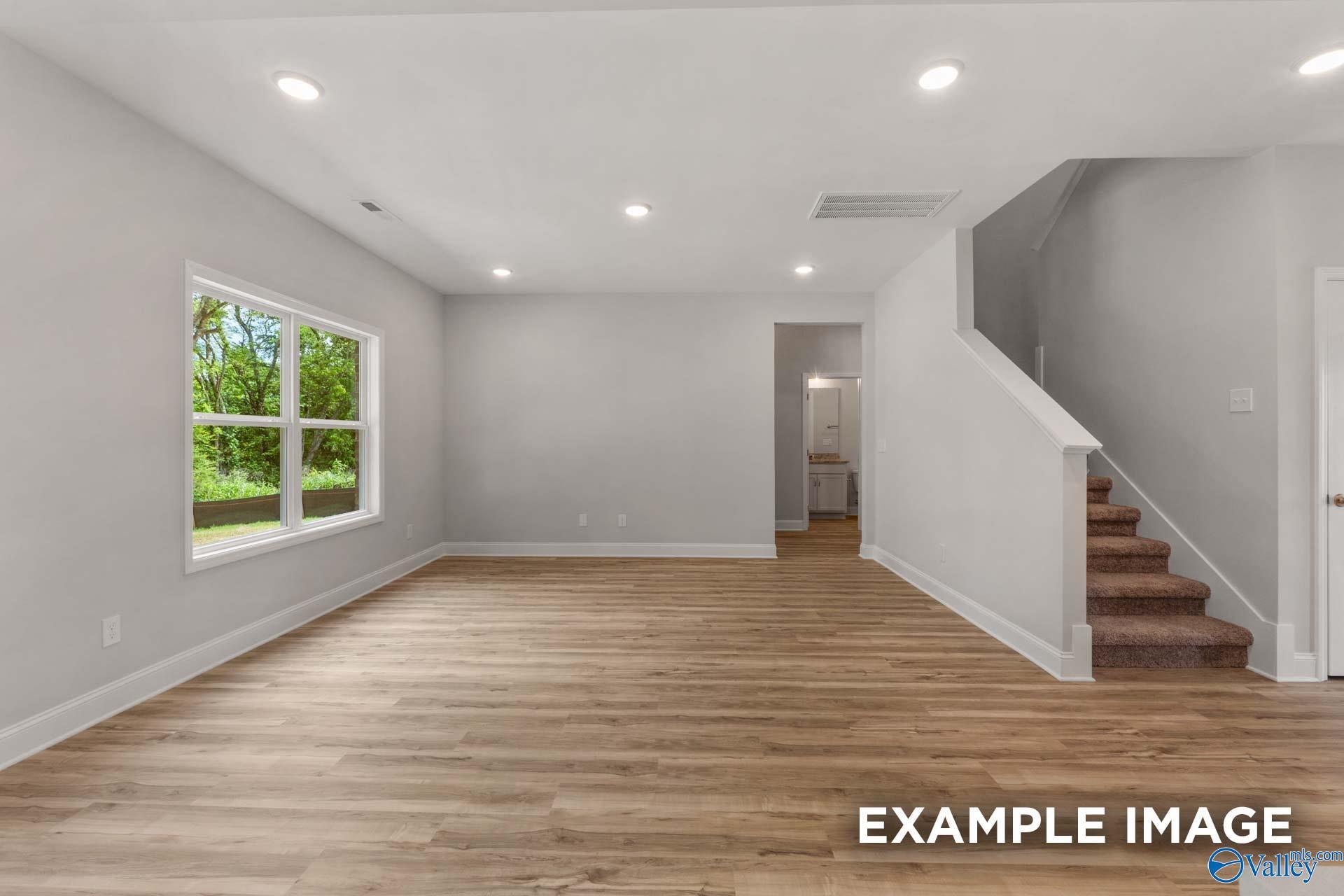 Bright open living room with hardwood floors, large windows, recessed lights, and carpeted staircase in Davidson Homes The Shelby C, Meridianville, Alabama