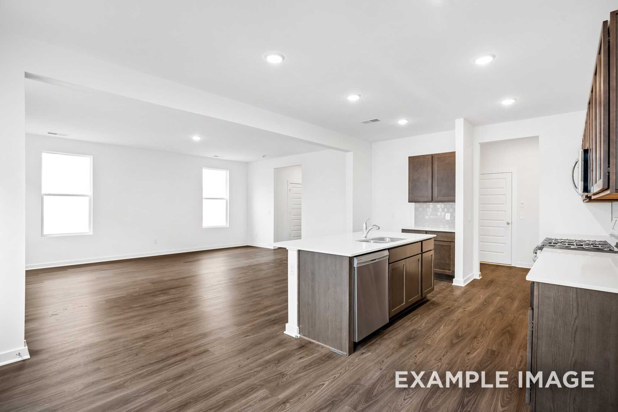 Spacious open-concept kitchen in The Grayson C with gray shaker cabinets, large white island, stainless appliances, and hardwood floors