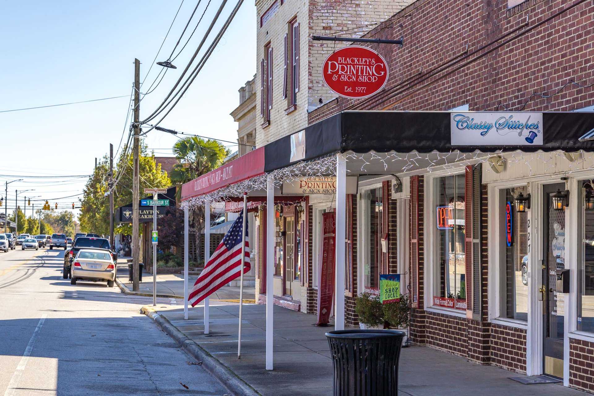 Charming brick storefronts on sunny Clayton NC street with American flags, Black's Painting shop, and bakery near Sierra Heights
