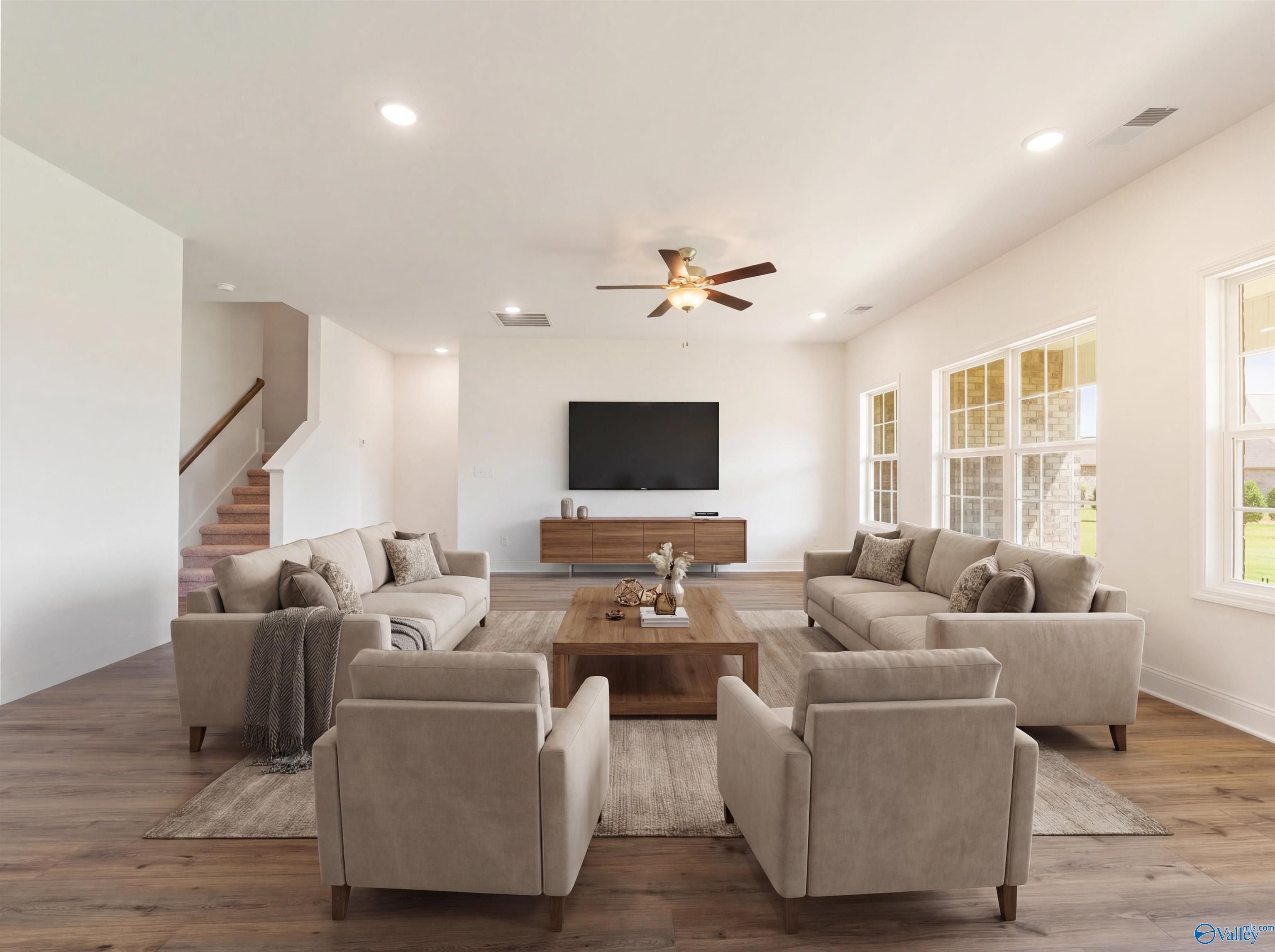 Spacious living room with beige sofas, wooden coffee table, wall TV, ceiling fan in Davidson Homes The Rockford B, Toney, Alabama