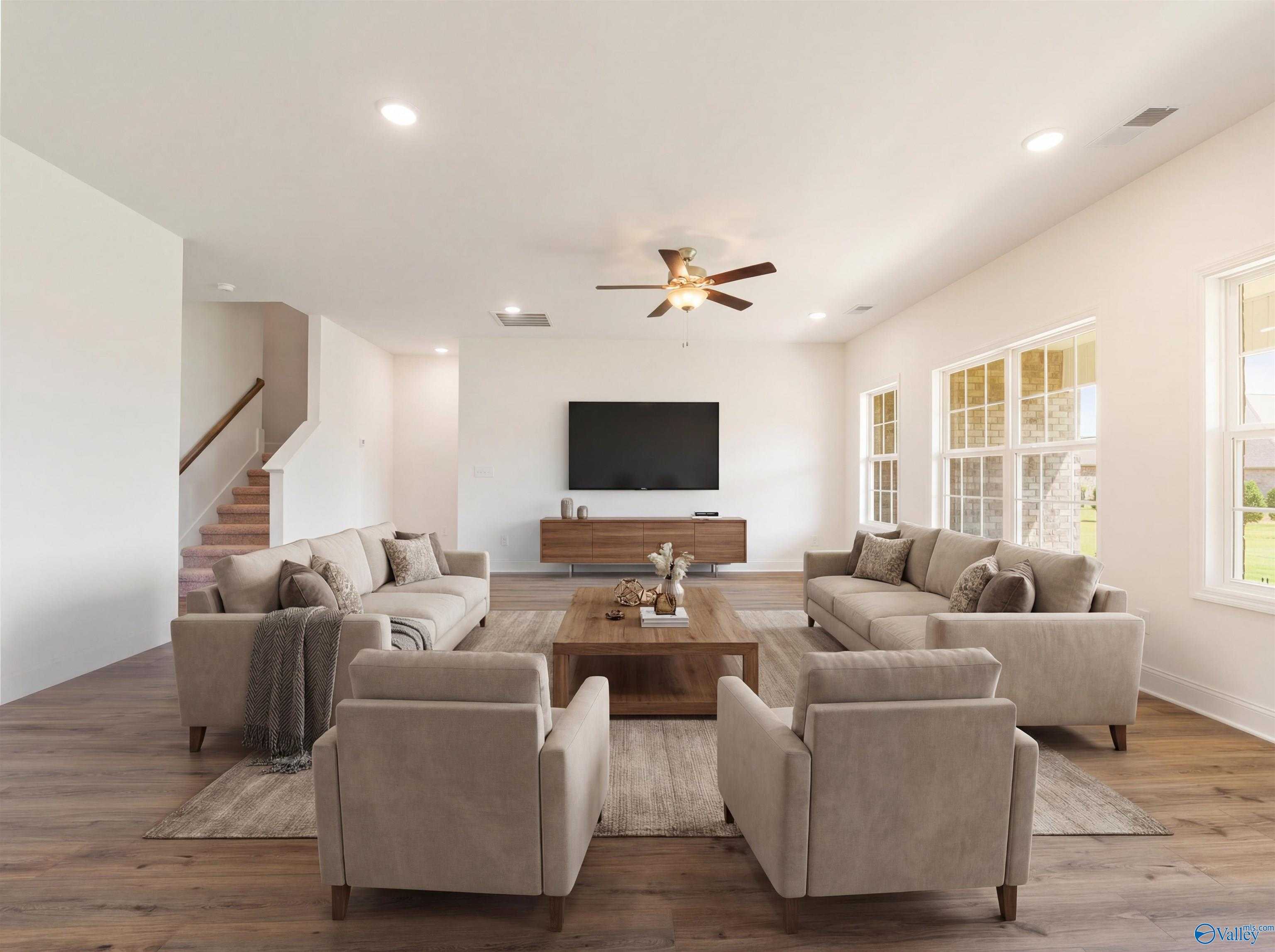 Spacious living room with beige sofas, wooden coffee table, wall TV, ceiling fan in Davidson Homes The Rockford B, Toney, Alabama