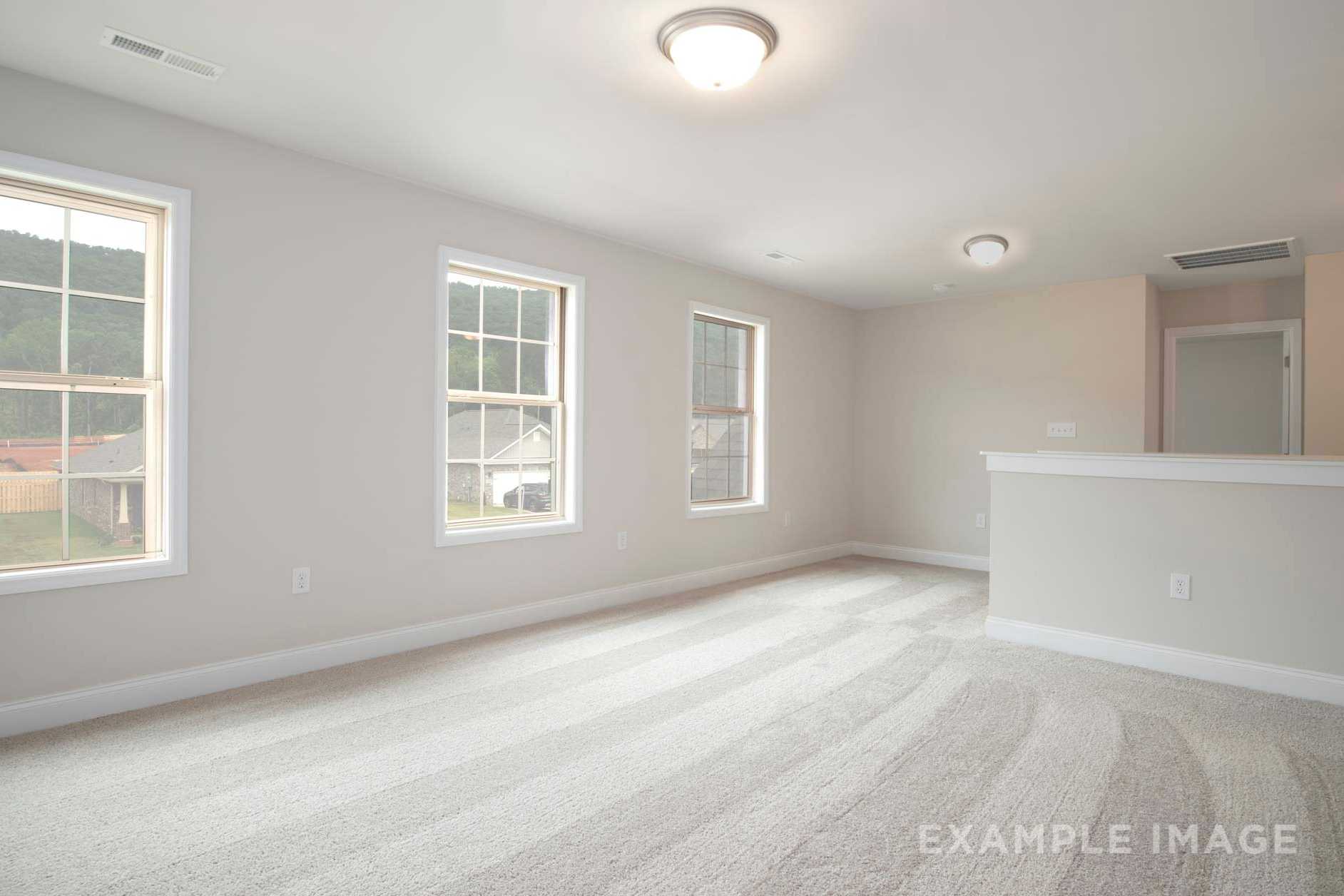 Spacious upper-floor bedroom in The Charleston with large windows overlooking woods, beige walls, carpeted floor