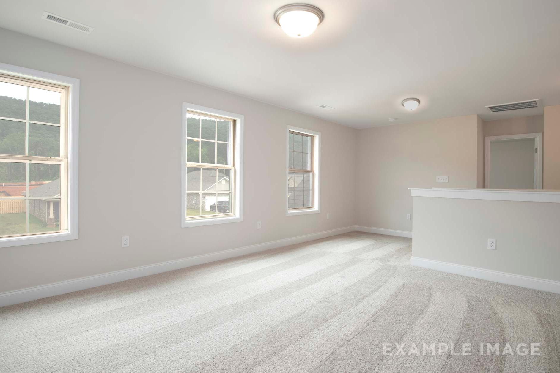 Spacious upper-floor bedroom in The Charleston with large windows overlooking woods, beige walls, carpeted floor