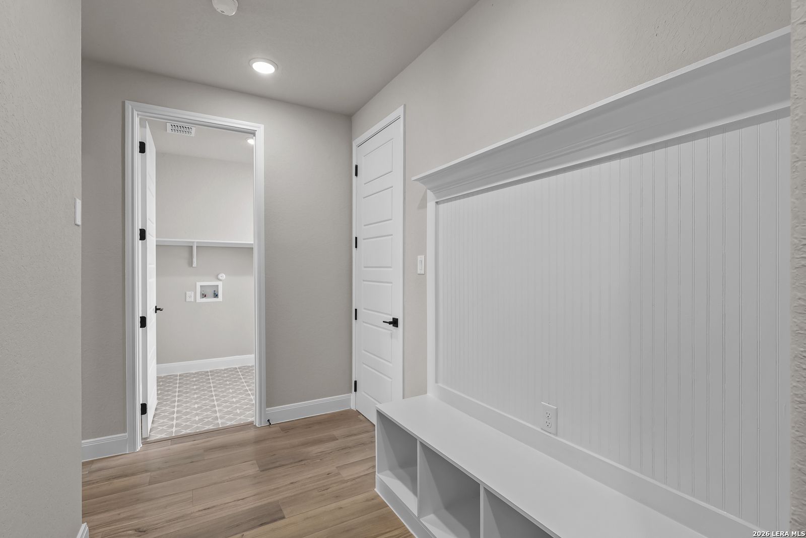 Mudroom with white beadboard accents, built-in bench cubbies, and view of laundry room in Davidson Homes Foster E plan, Castroville, TX