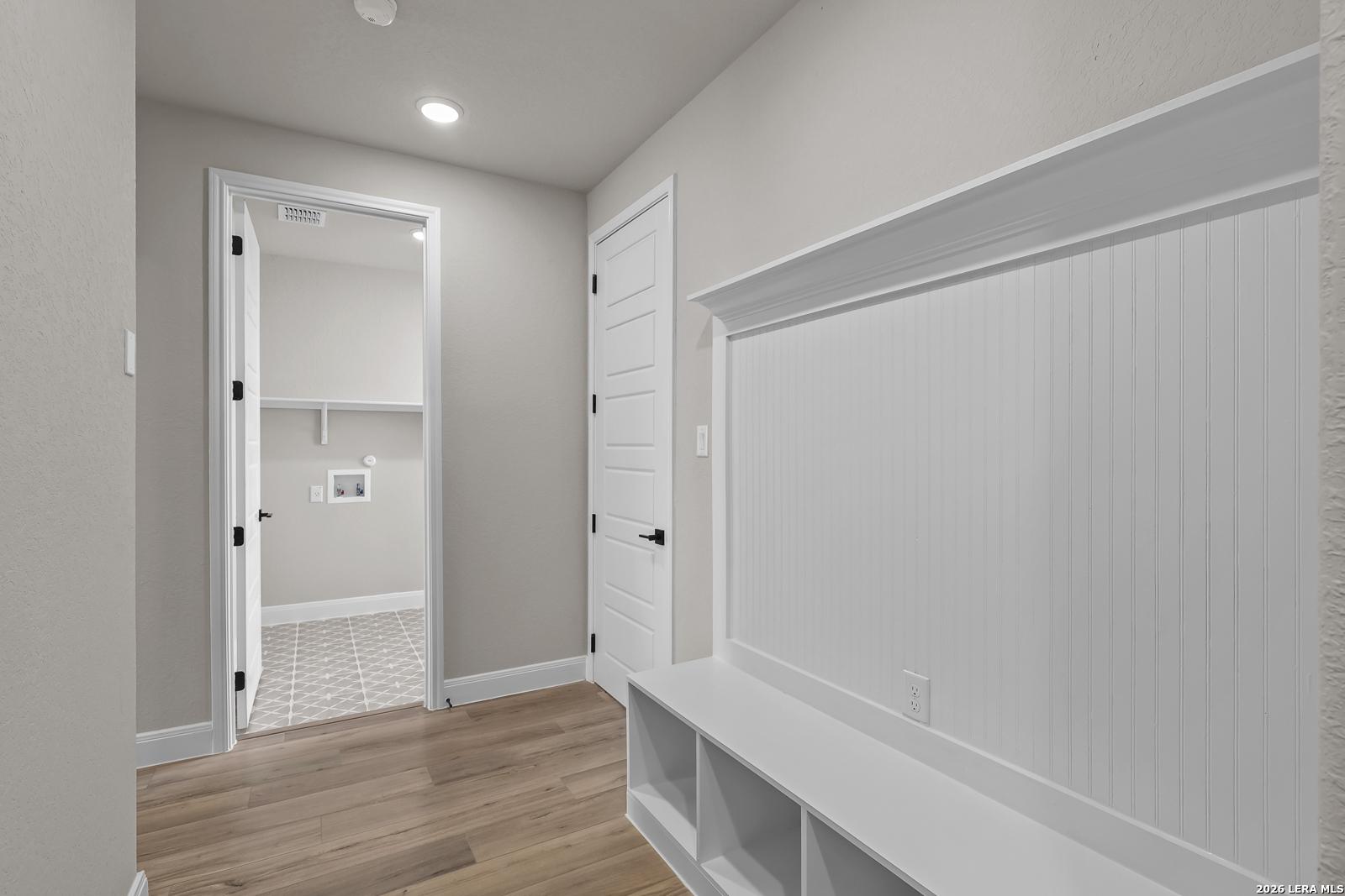 Mudroom with white beadboard accents, built-in bench cubbies, and view of laundry room in Davidson Homes Foster E plan, Castroville, TX