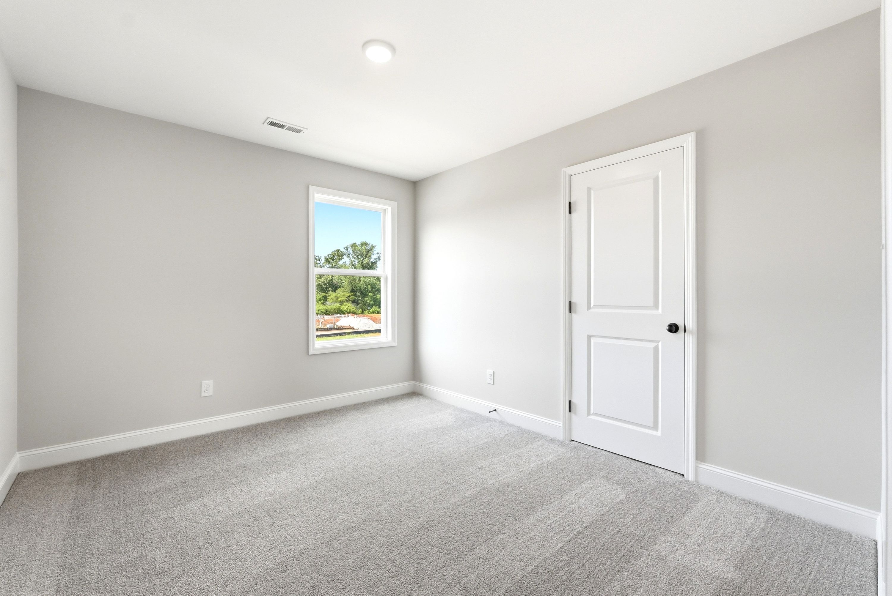 Spacious, light-filled bedroom in The Russell A floor plan featuring neutral paint, plush carpeting, and a single window.