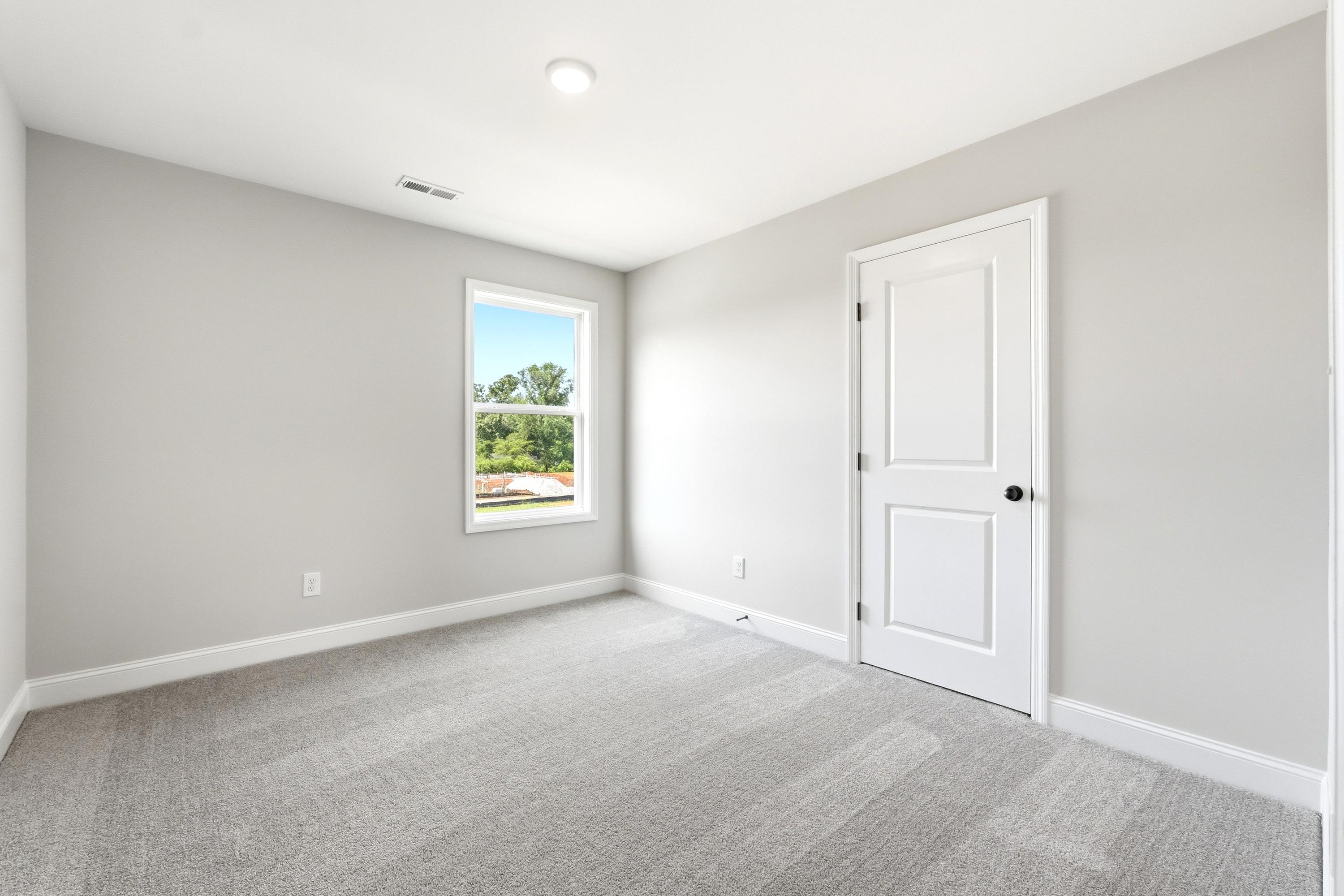 Spacious, light-filled bedroom in The Russell A floor plan featuring neutral paint, plush carpeting, and a single window.