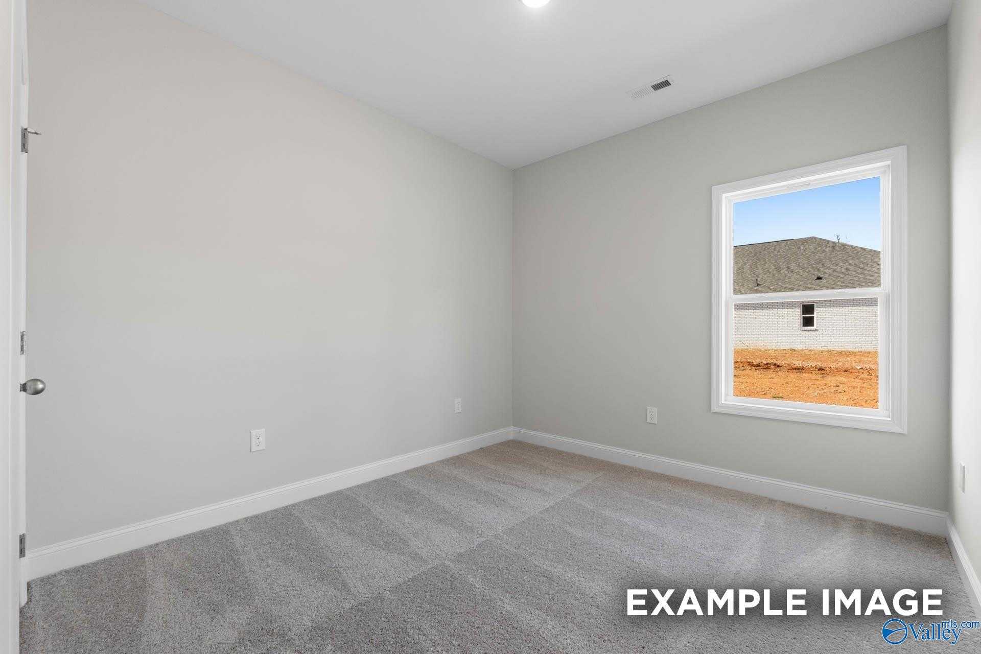 Spacious empty secondary bedroom with light gray walls, plush carpet, and window overlooking construction in The Butler, Huntsville AL