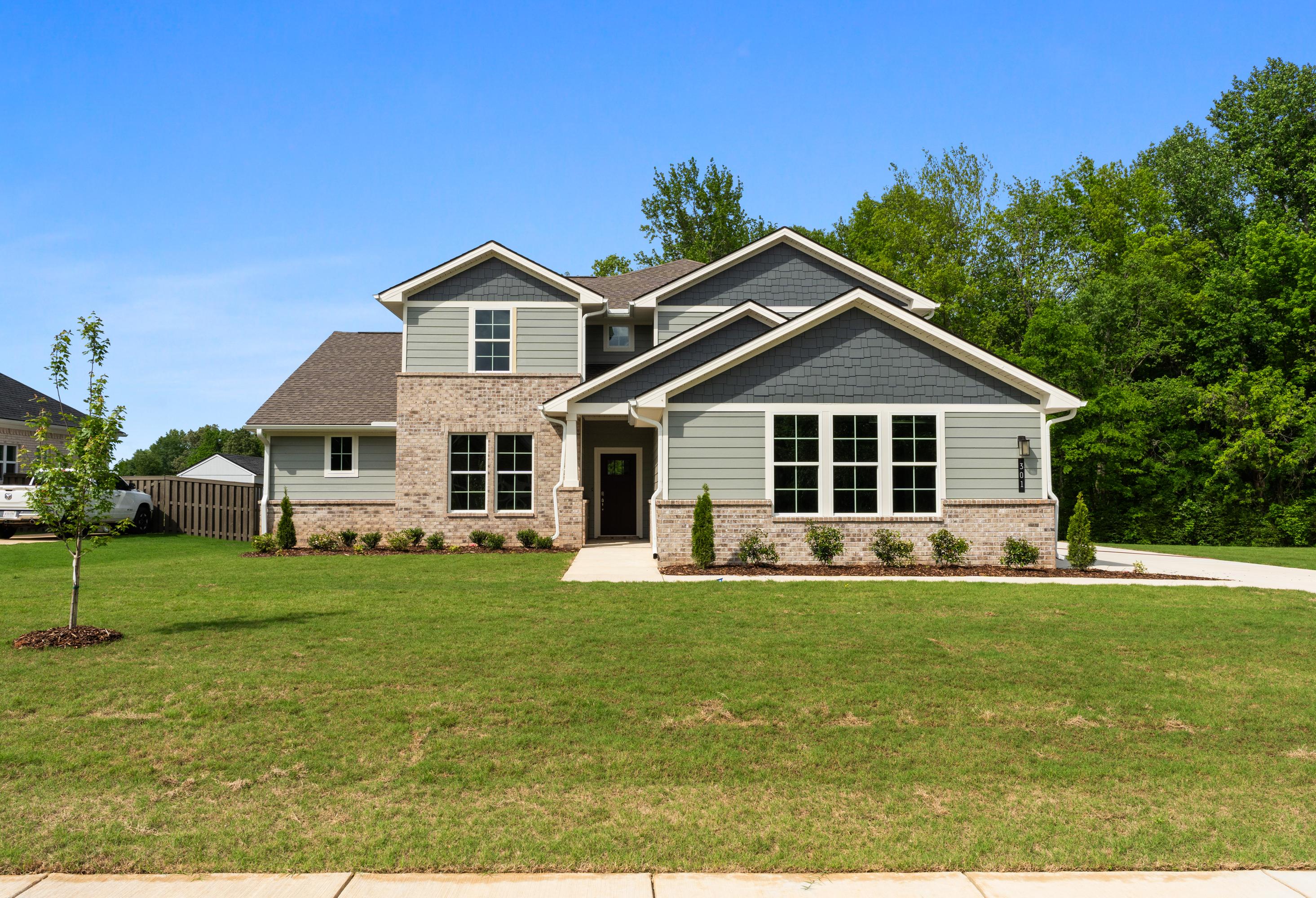 Two-story Avalon D home exterior with gray siding, brick accents, large windows, and landscaped yard in Owens Cross Roads