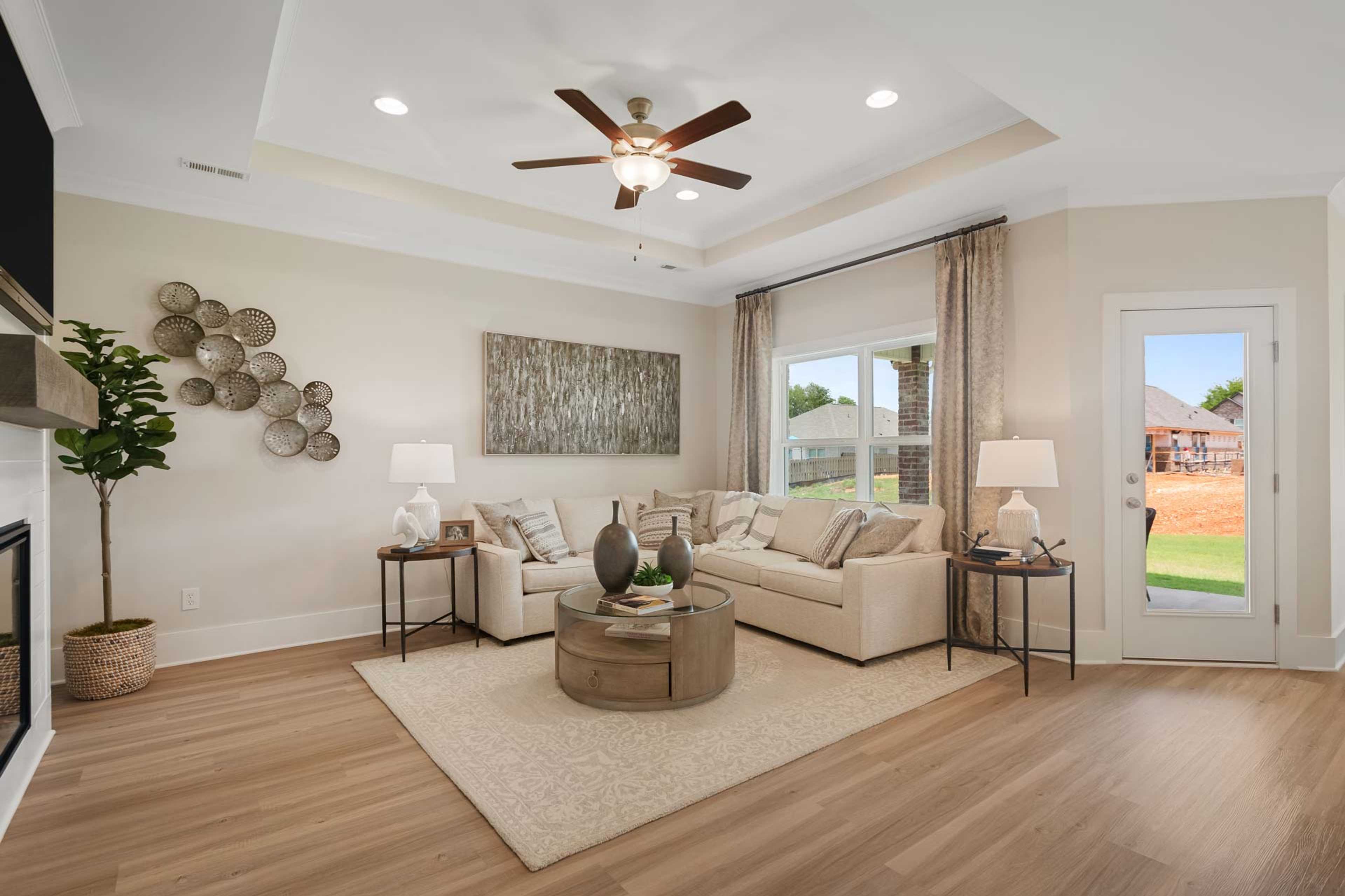 Cozy living room at Flint Meadows in New Market Alabama with beige sofas, fireplace, ceiling fan, and backyard view