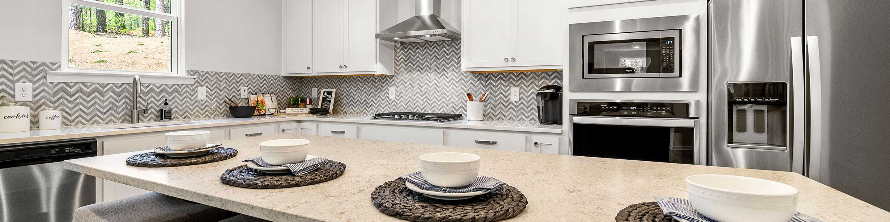 Spacious white kitchen in Riverwood Dallas GA by Davidson Homes with shaker cabinets, stainless appliances, chevron backsplash, and island bar seating