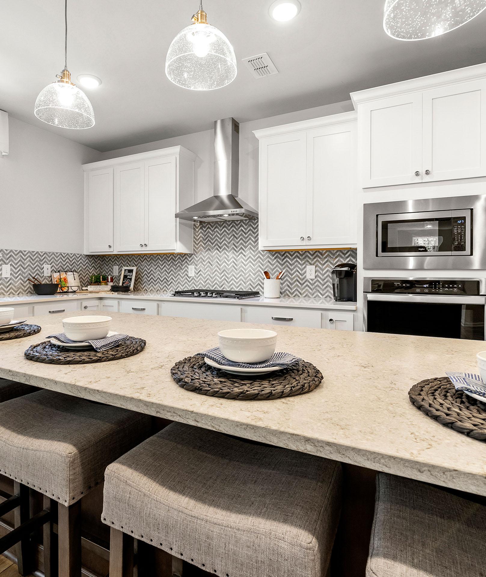 Spacious white kitchen in Riverwood Dallas GA by Davidson Homes with shaker cabinets, stainless appliances, chevron backsplash, and island bar seating