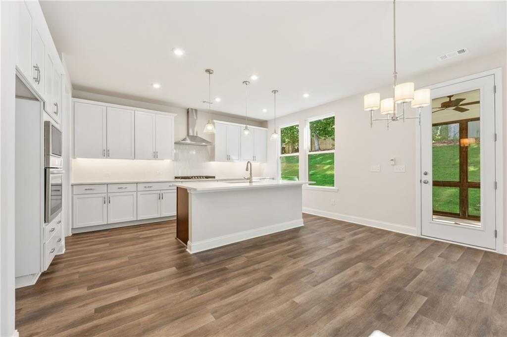 Modern kitchen with white cabinets, large island sink, stainless appliances, hardwood floors, and French doors to backyard in The Danbury E, Buford, GA