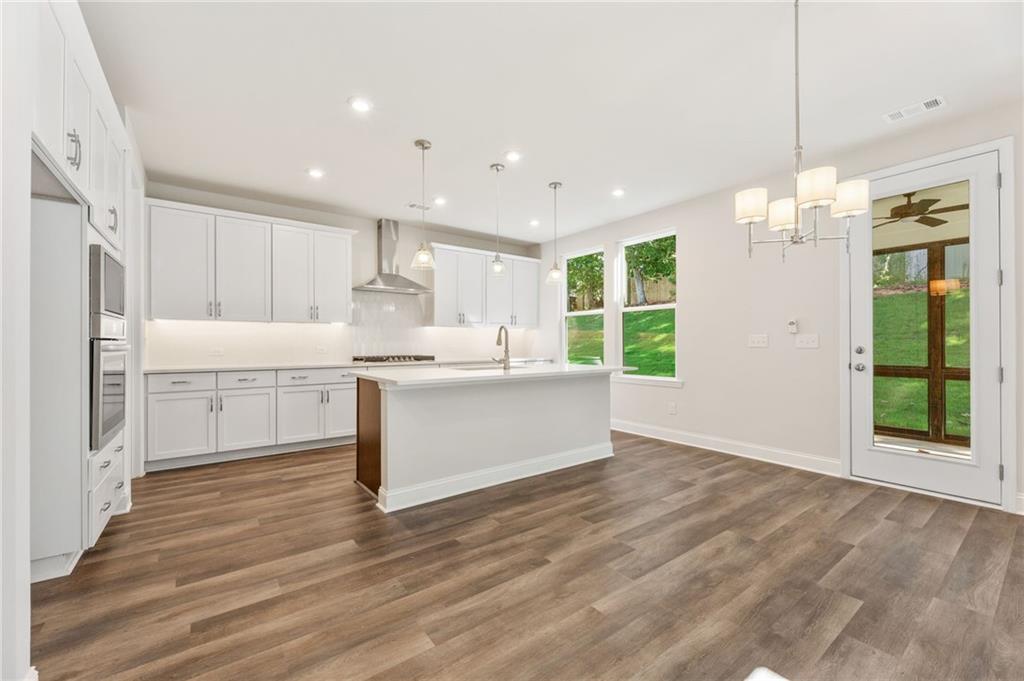 Modern white kitchen with large island, stainless appliances, hardwood floors in The Danbury E, Buford, Georgia