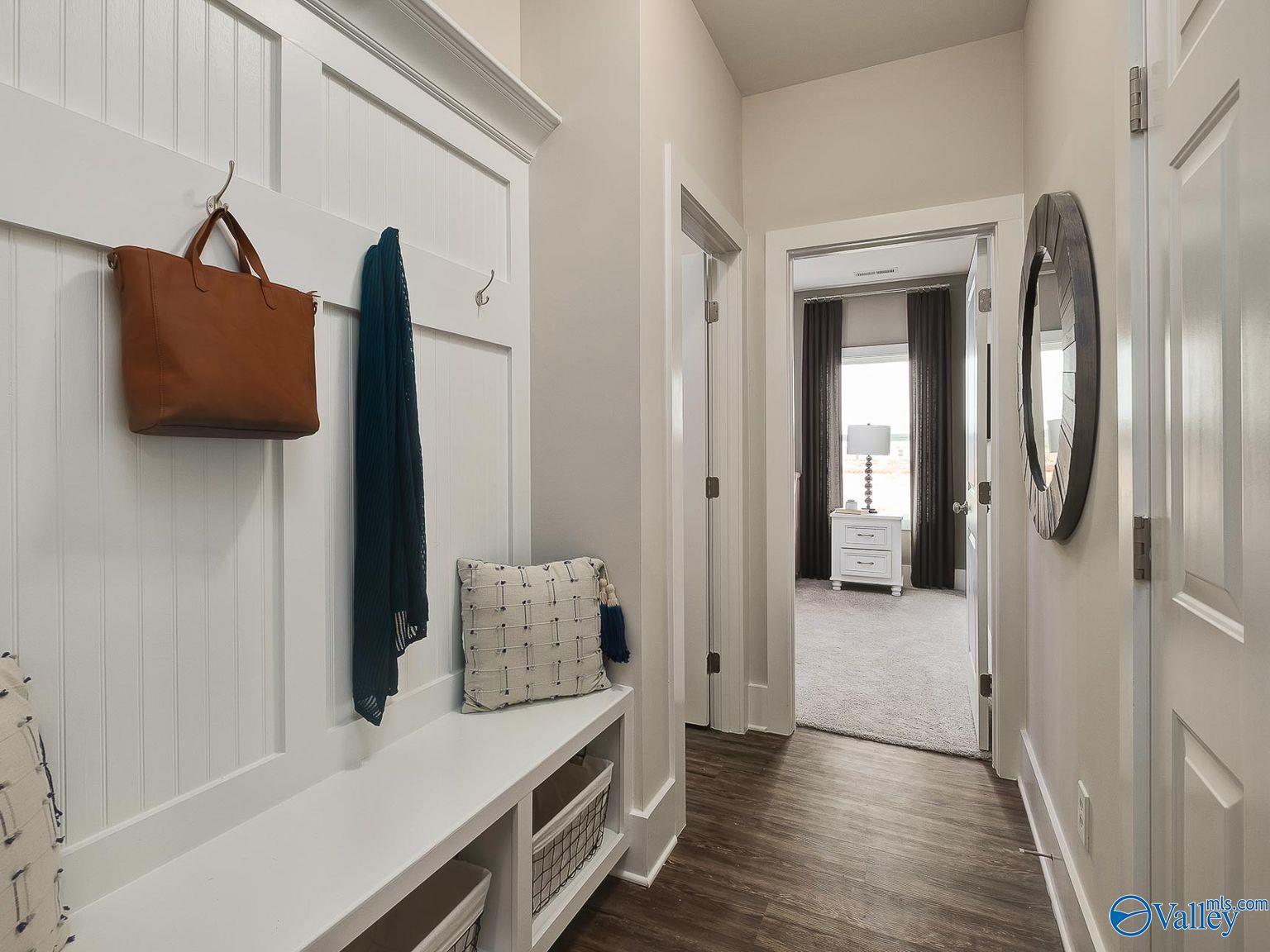 Spacious mudroom with white shiplap walls, built-in bench, coat hooks, handbag, and wicker storage leading to bedroom in Davidson Homes The Everett, Toney, Alabama