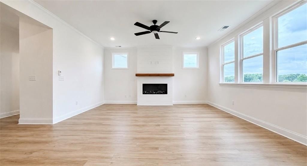 Bright living room with shiplap fireplace, wood floors, and ceiling fan in Davidson Homes The Hickory C, Hoschton, GA.