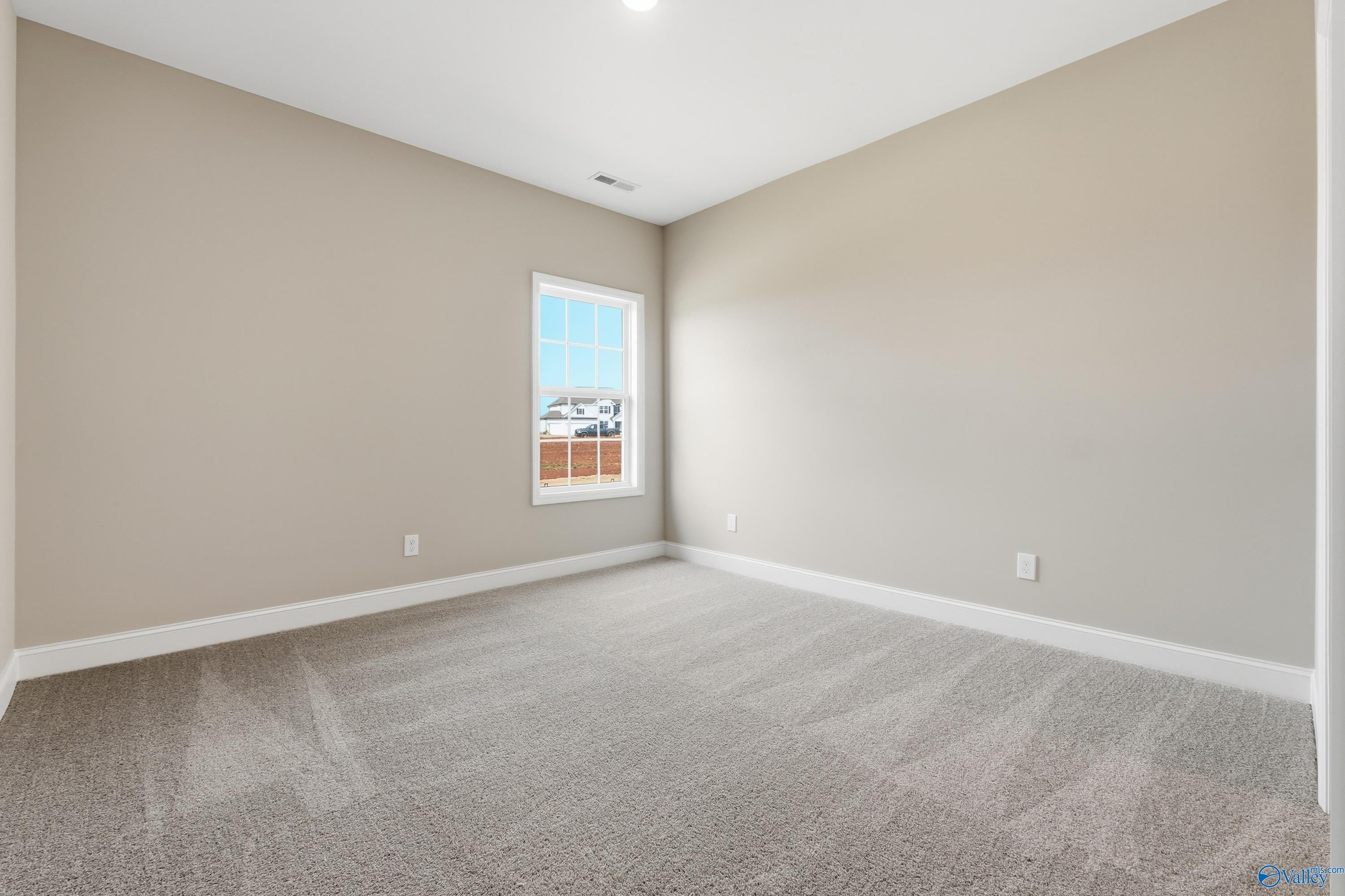 Bright empty secondary bedroom with beige walls, large window, and carpeted floor in Davidson Homes The Lanier, Meridianville, Alabama