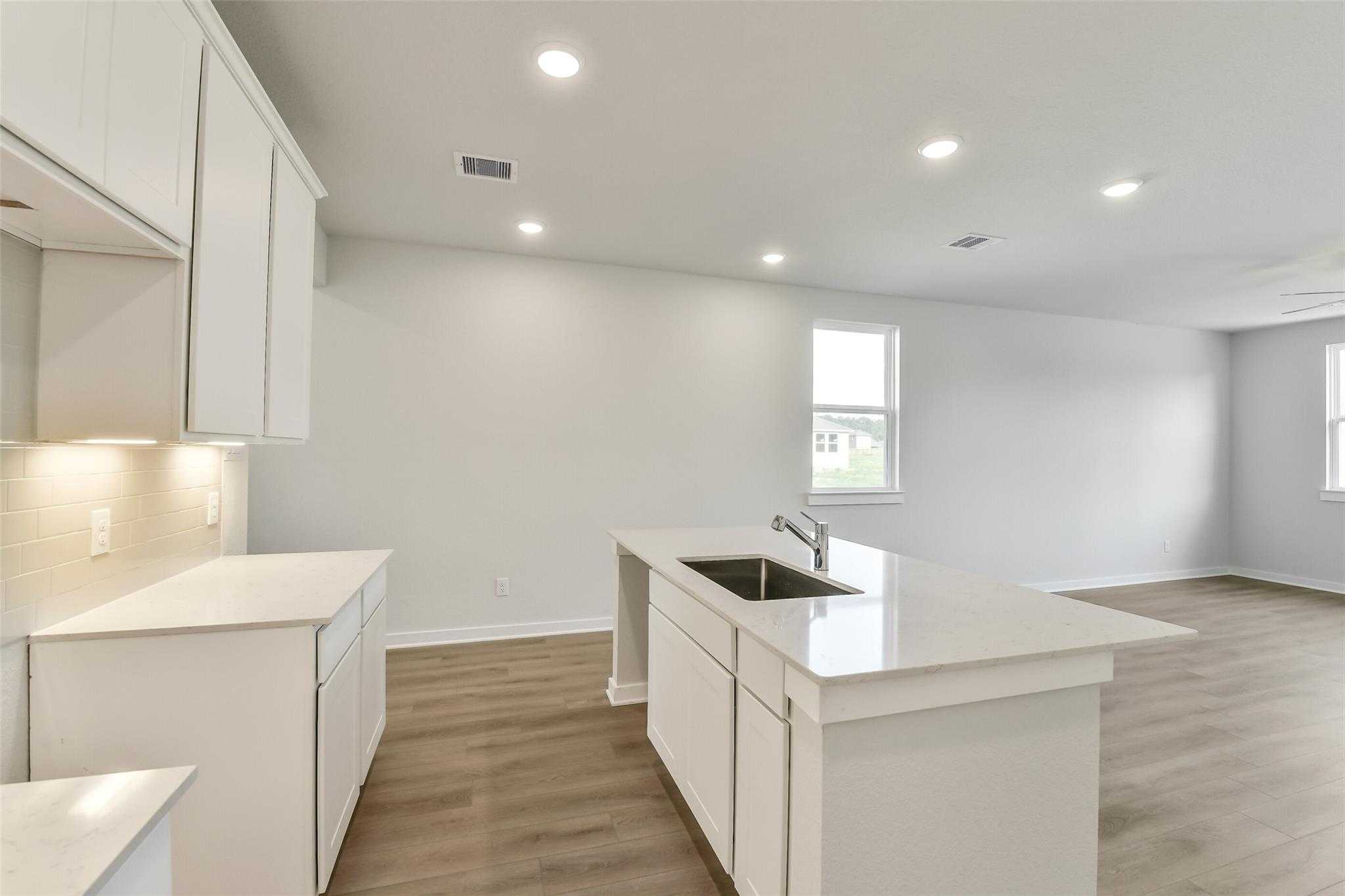 Modern white kitchen with quartz island sink and shaker cabinets in Davidson Homes The Colorado F, Cleveland, Texas