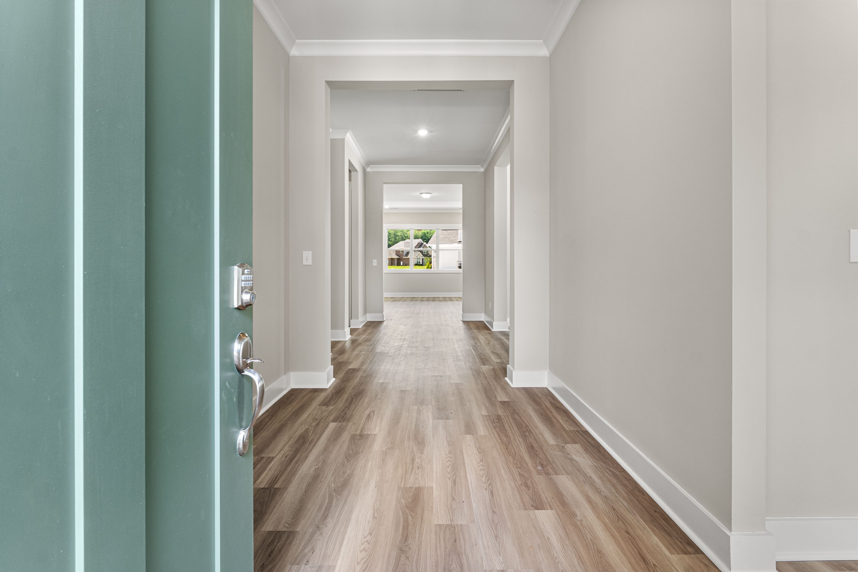 Spacious entry hallway in The Oxford A home with open teal door, light oak floors, neutral walls, and natural light