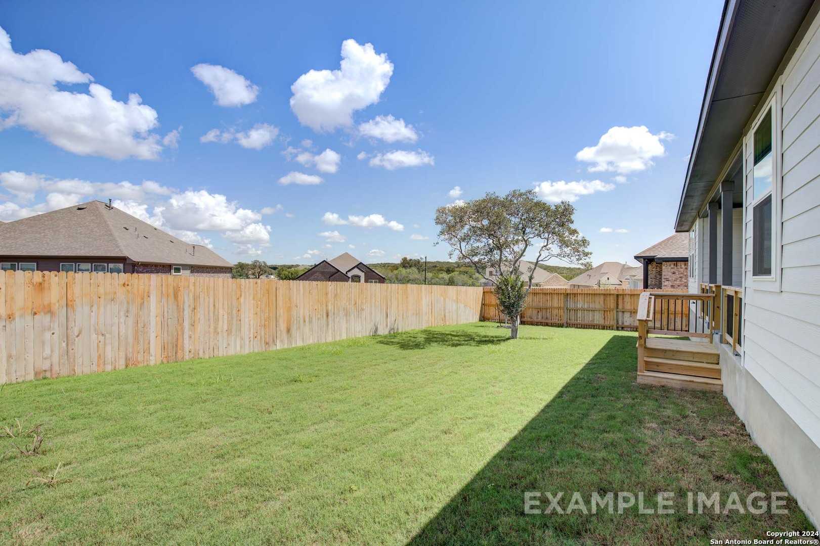 Private fenced backyard with lush green lawn, wooden deck, and tree in Davidson Homes The Rockford G, Ladera, San Antonio