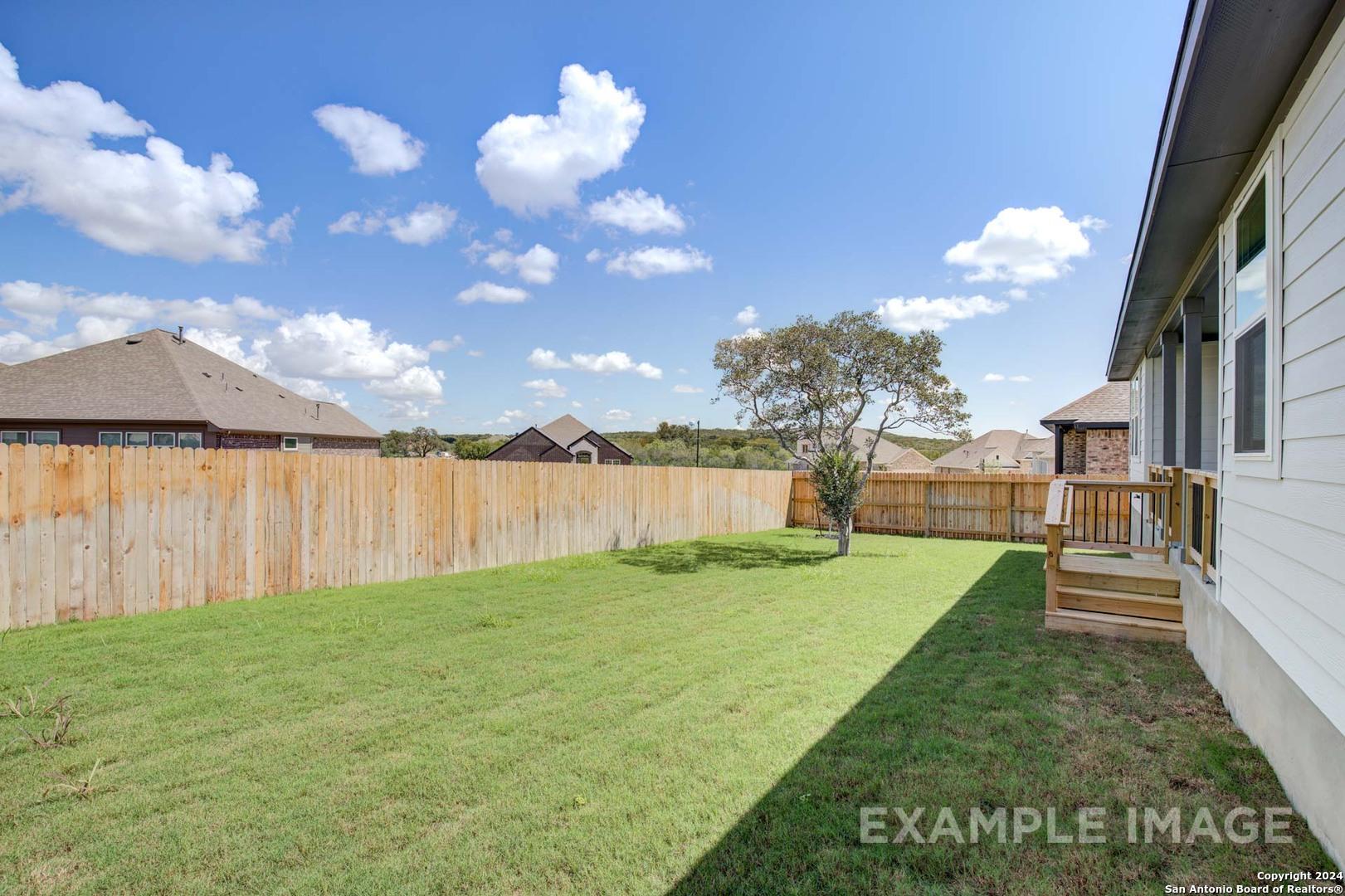Private fenced backyard with lush green lawn, wooden deck, and tree in Davidson Homes The Rockford G, Ladera, San Antonio