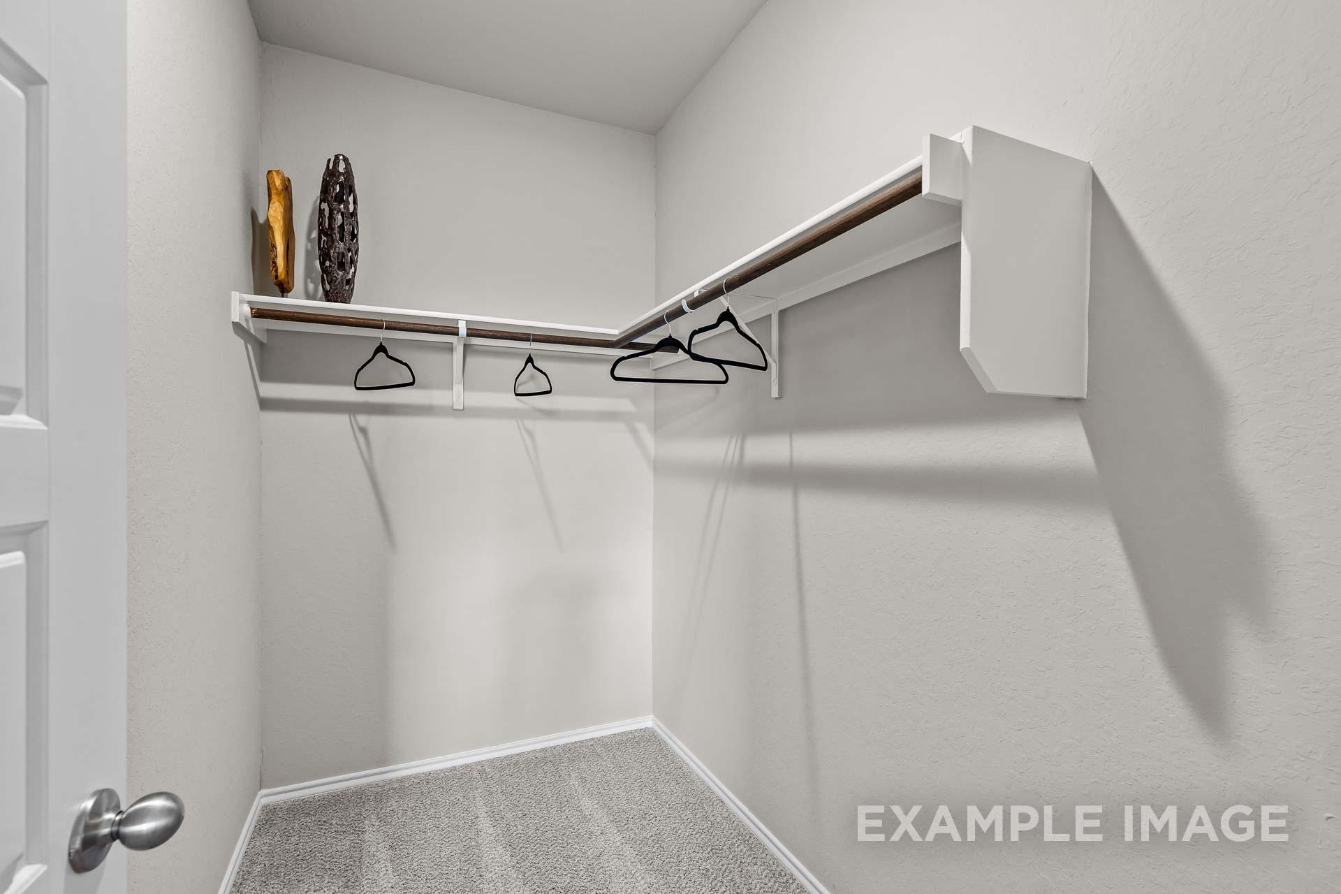 Spacious walk-in closet with wooden shelves, hanging rods, and decorative accents in master suite of Davidson Homes The Sabine J, Heartland, Texas